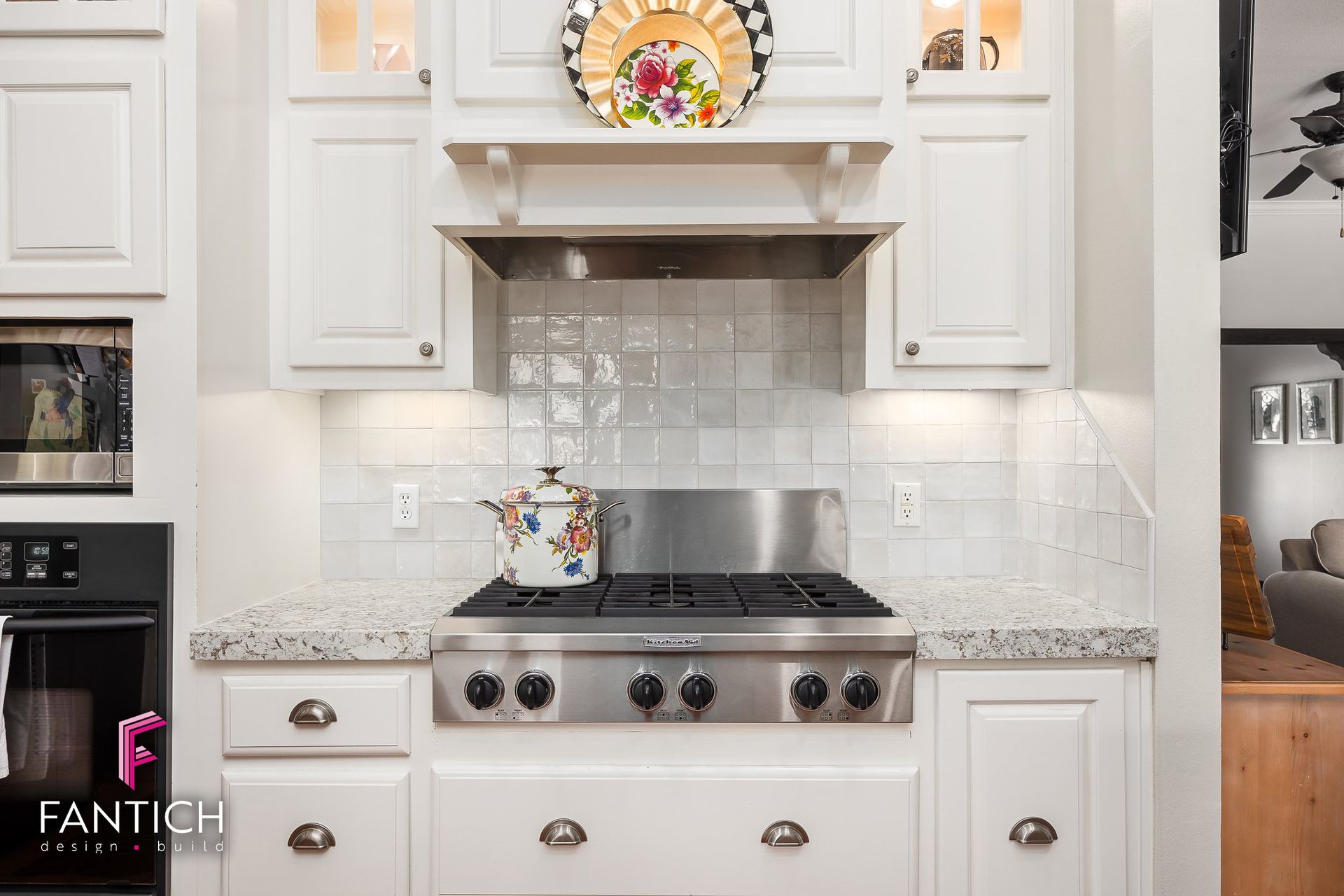 White kitchen with stainless steel stove, white cabinets, granite countertops, and decorative backsplash tile.
