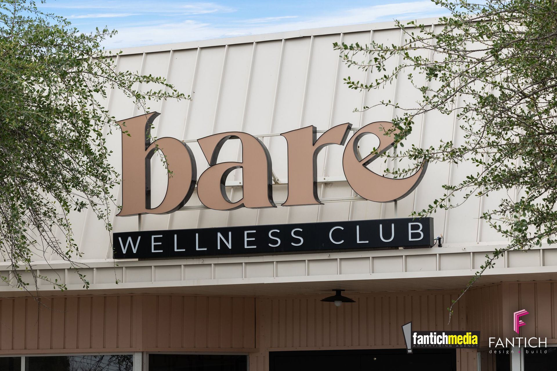 Bare Wellness Club sign on a building facade, with trees framing the entrance.