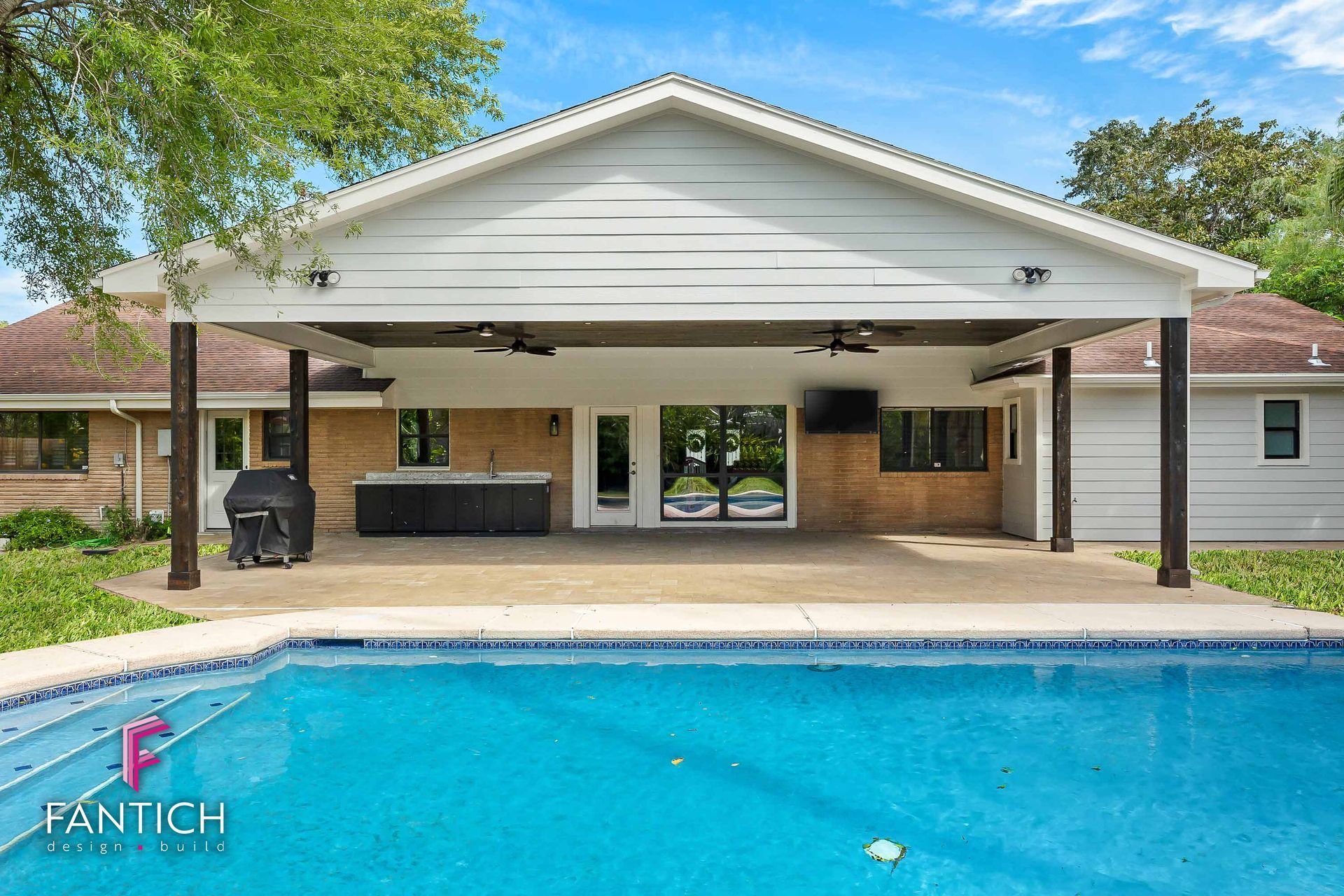 Backyard pool with covered patio and brick house in the background