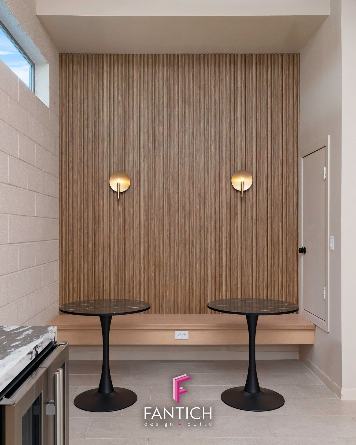 Modern lounge with striped wall, two round tables, wall sconces, and a bench