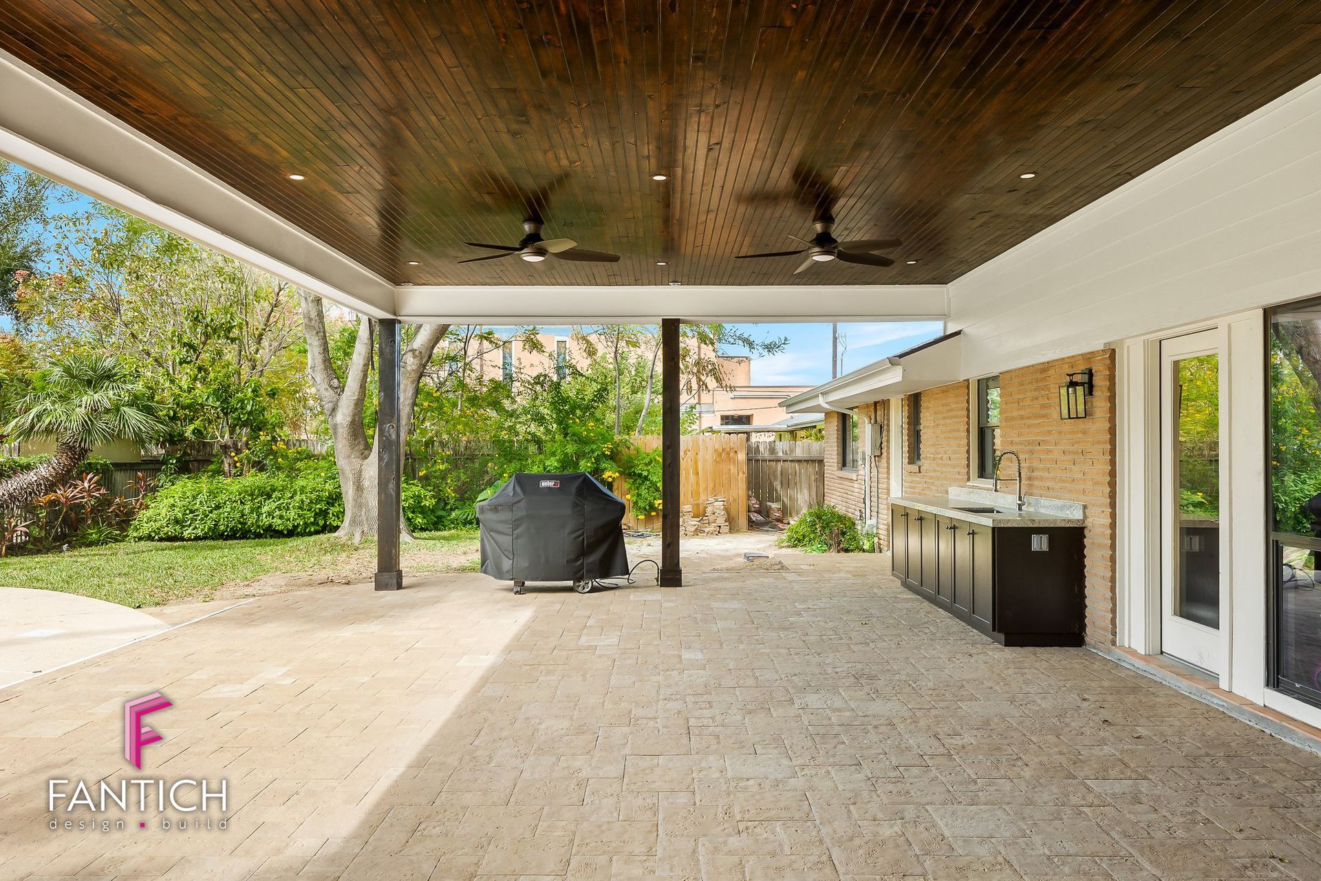 Covered patio with ceiling fans, grill, and outdoor cabinets beside a backyard lawn