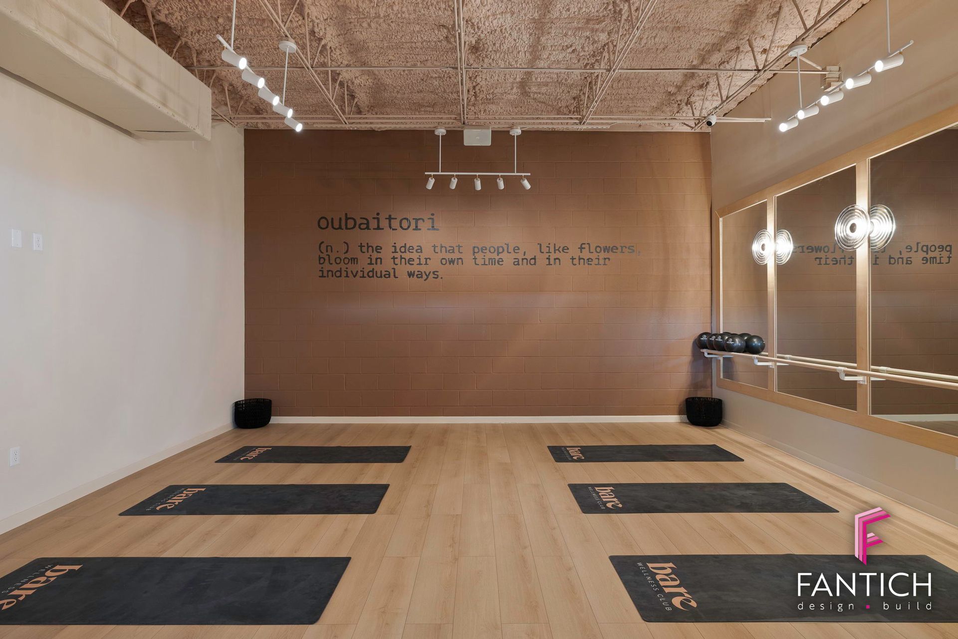 Empty yoga studio with wooden floor, wall mirrors, mats laid out, and soft lighting