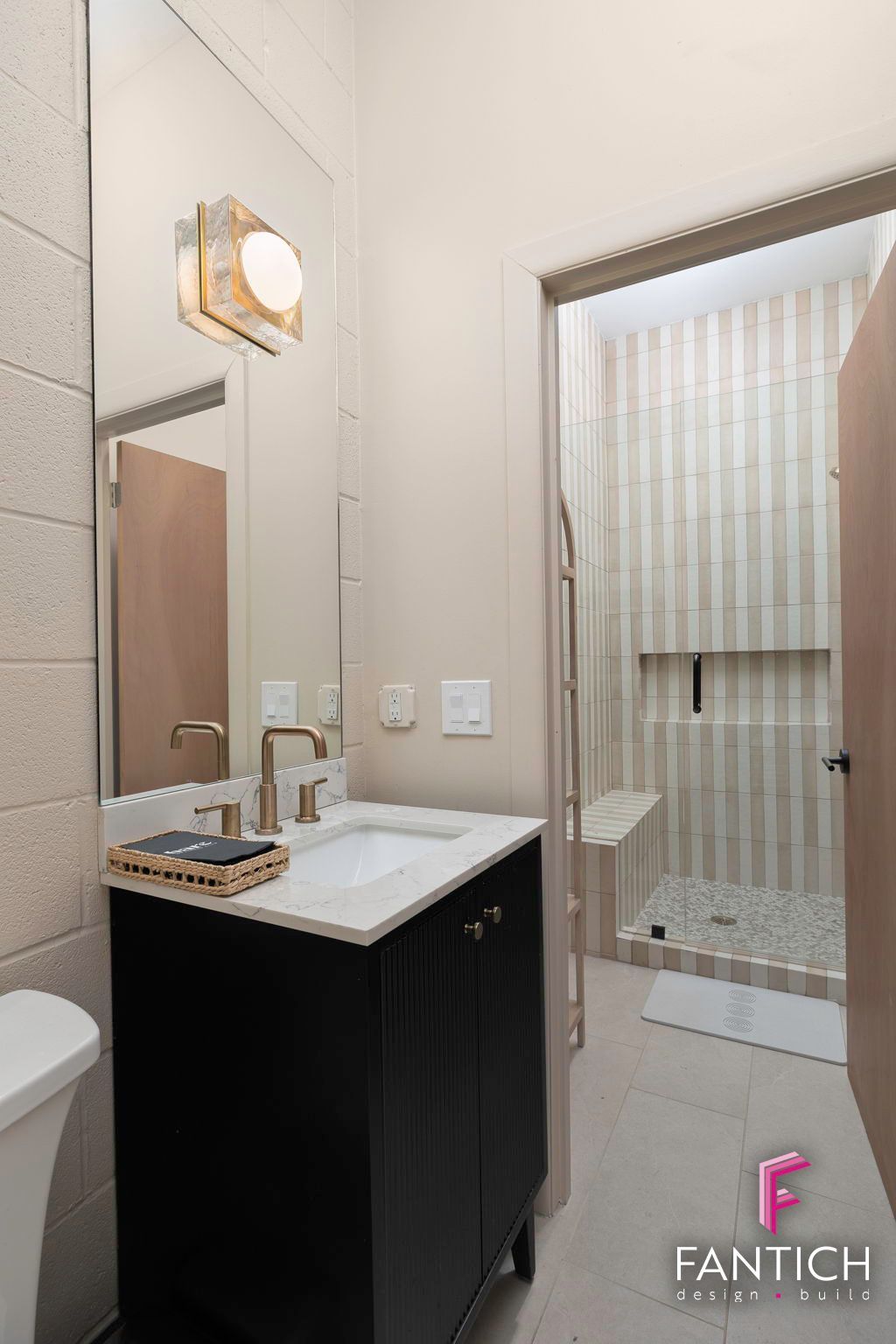 Compact bathroom vanity with black cabinet, white sink, mirror, and glass shower door with striped curtain