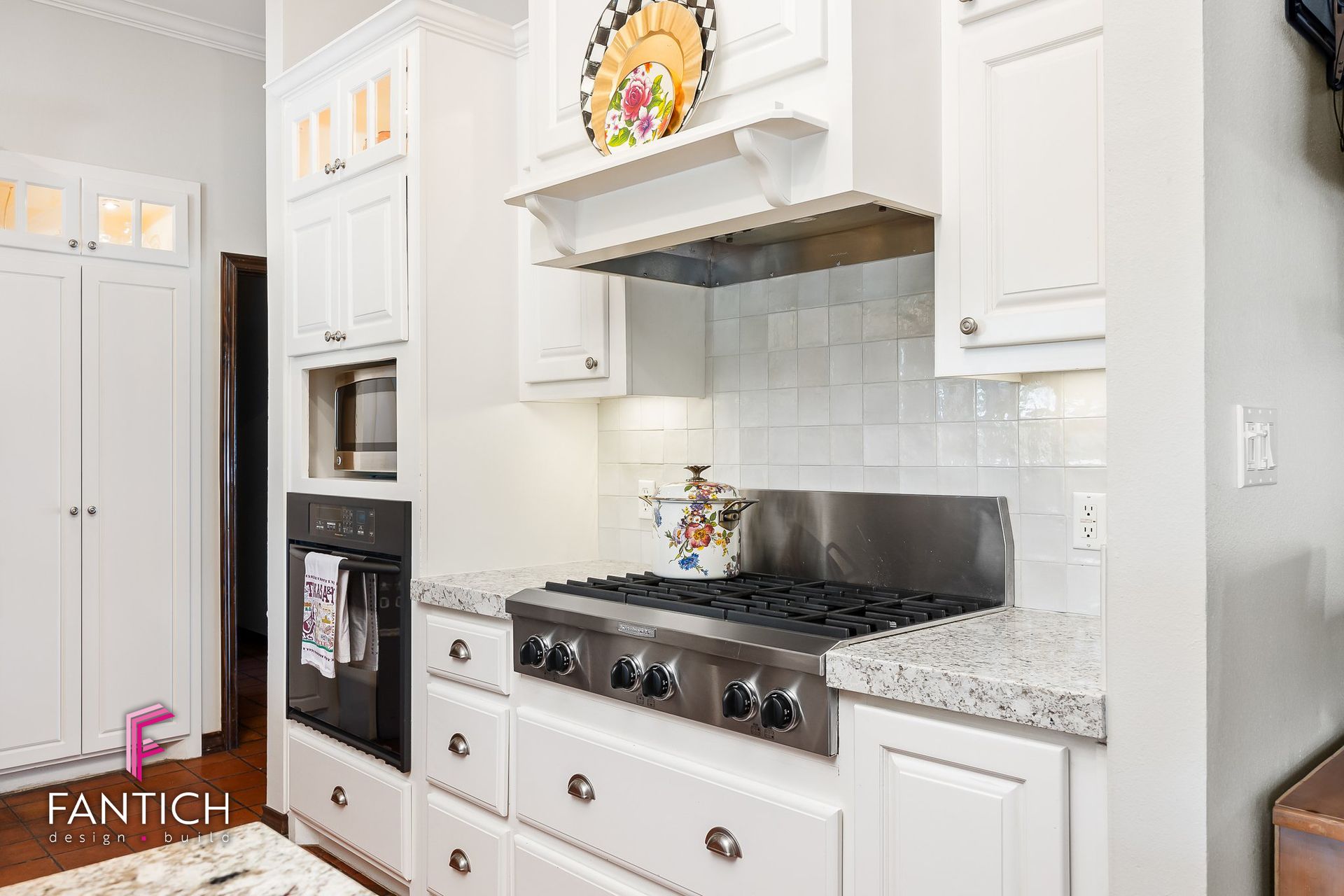 Bright white kitchen with stainless stove, granite counters, tiled backsplash, and built-in oven cabinet.