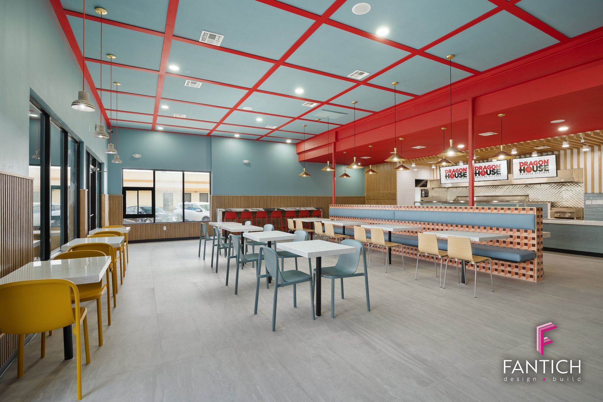 Modern cafeteria with red ceiling grid, blue walls, and tables and chairs in a bright open space