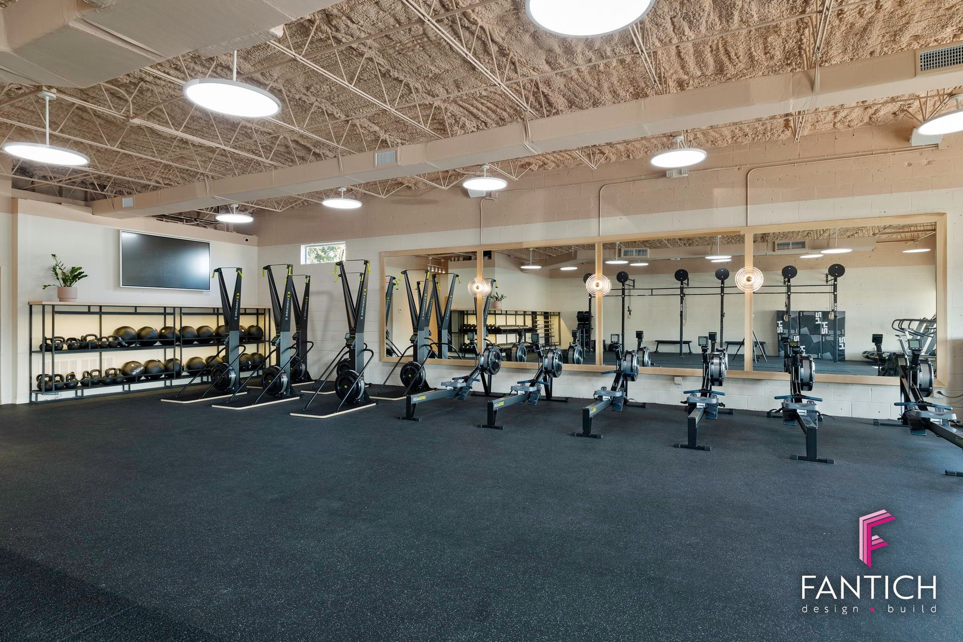 Spacious gym with weight racks, benches, and exercise equipment on black flooring under exposed ceiling lights