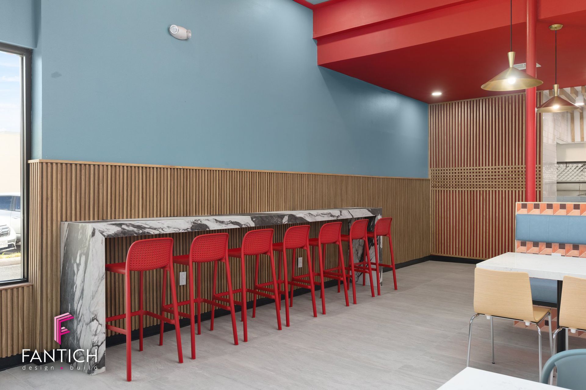 Modern cafe interior with red bar stools, blue walls, wood paneling, and pendant lights
