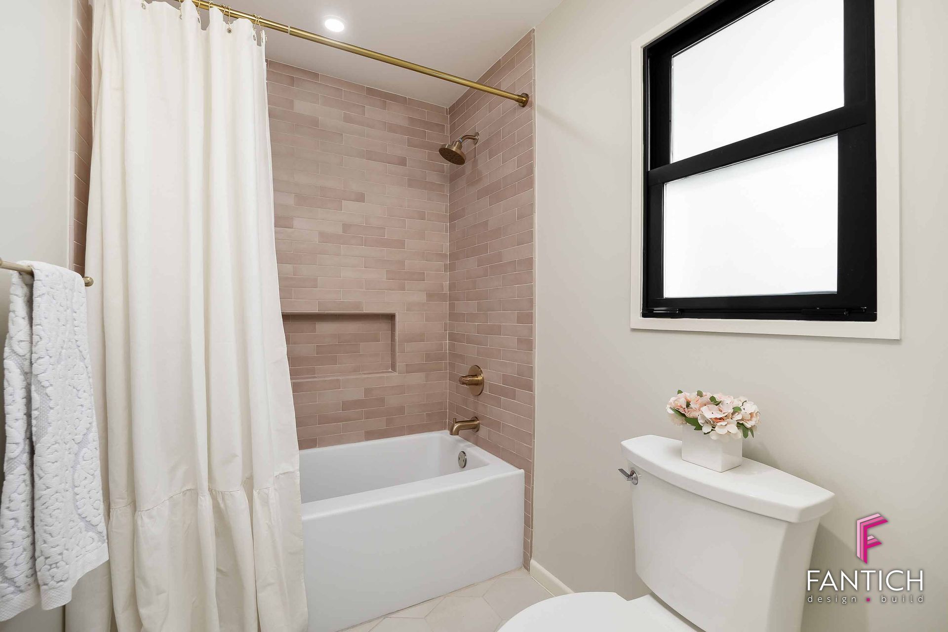 Modern bathroom with white tub, tiled shower, black-framed window, and toilet
