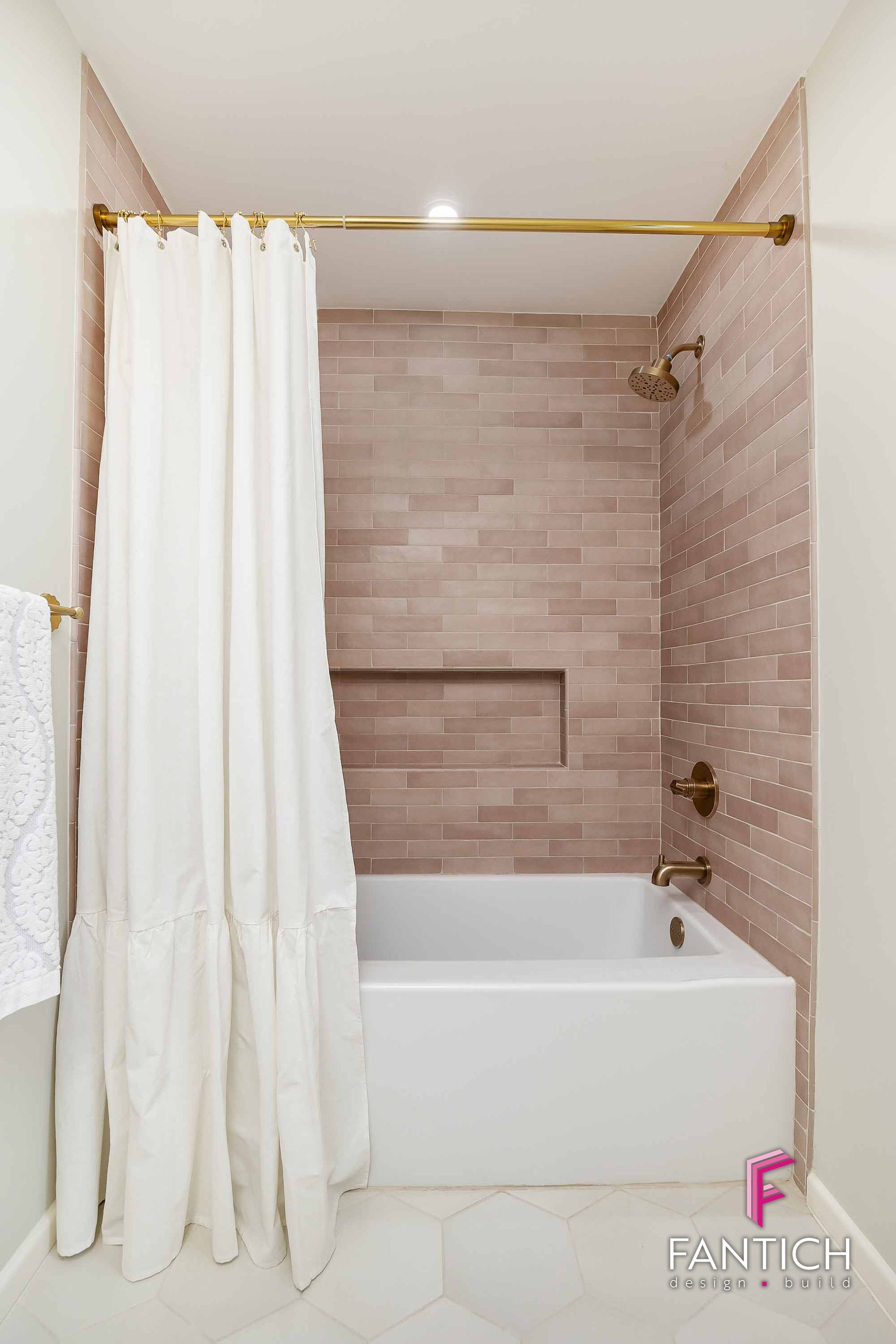 Modern bathroom with white tub, beige tiled shower wall, and white curtain on a gold rod