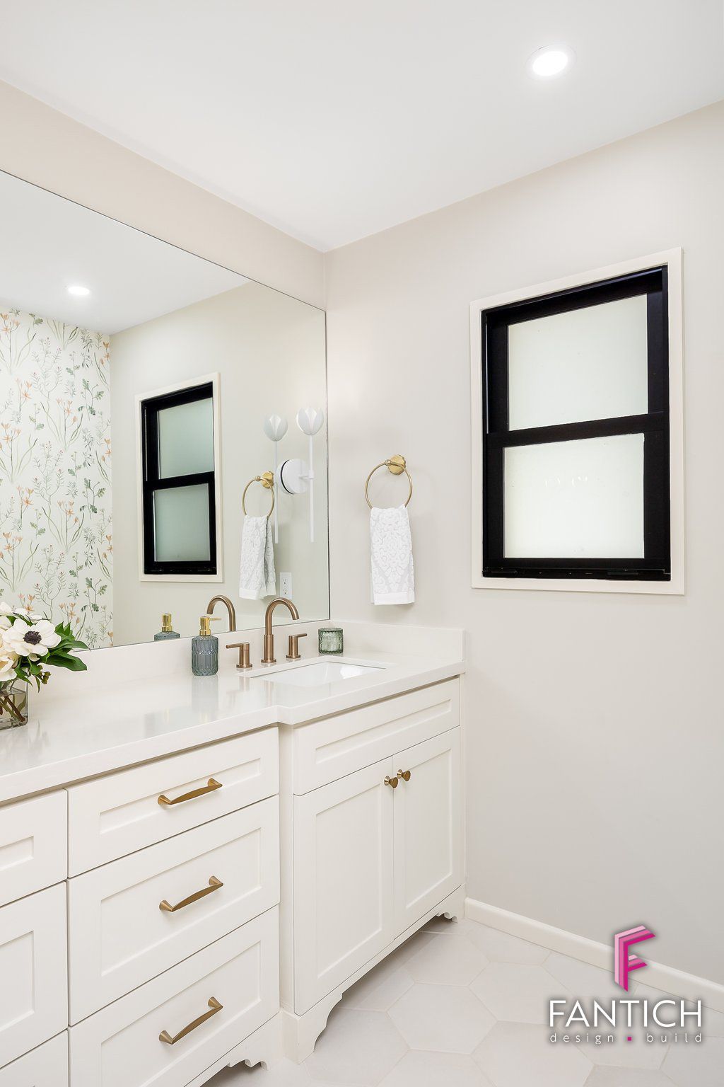 Bright white bathroom vanity with gold fixtures, wall mirror, and black-framed window