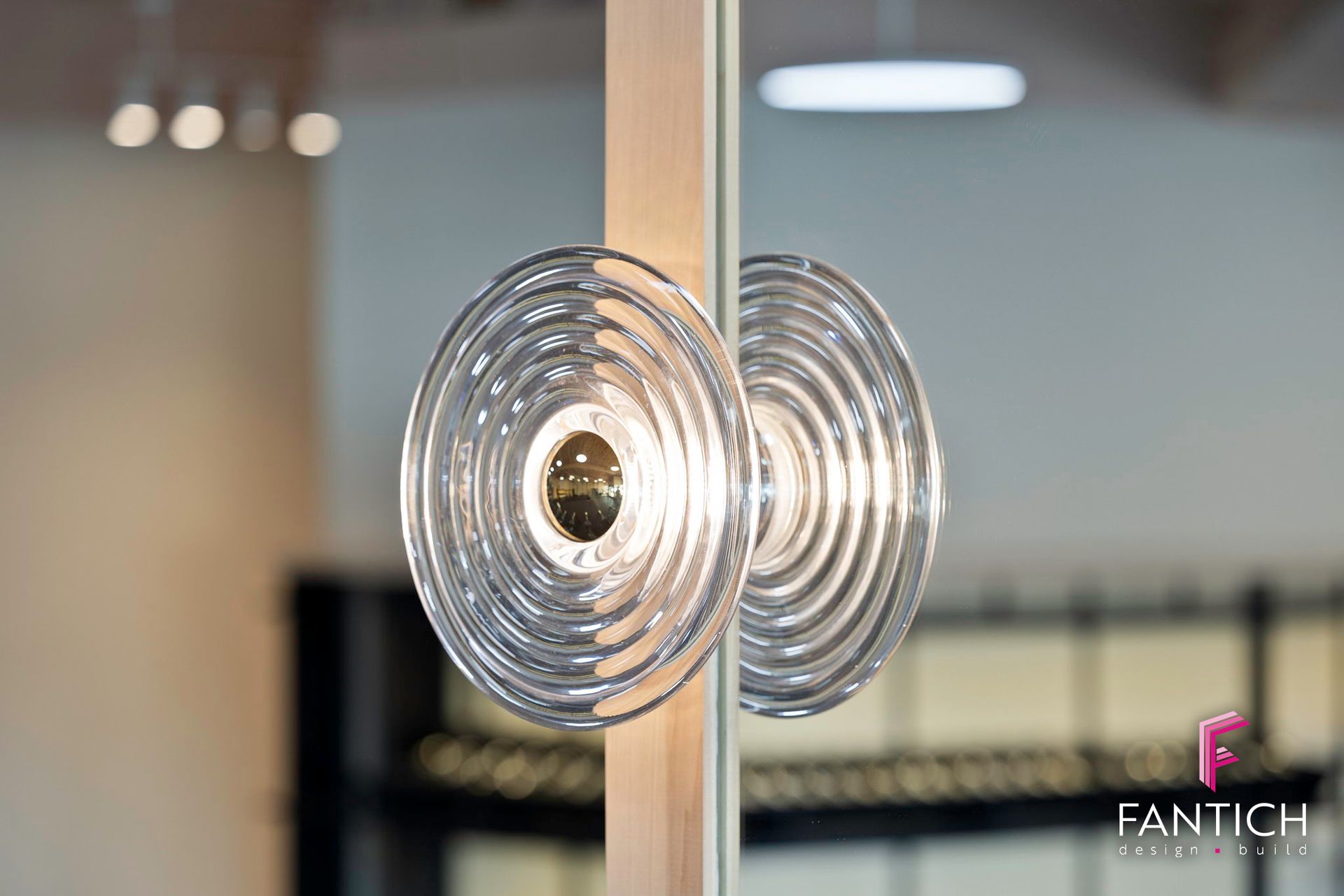Two clear spiral glass door handles on a wooden-framed glass door, with a blurred interior background.