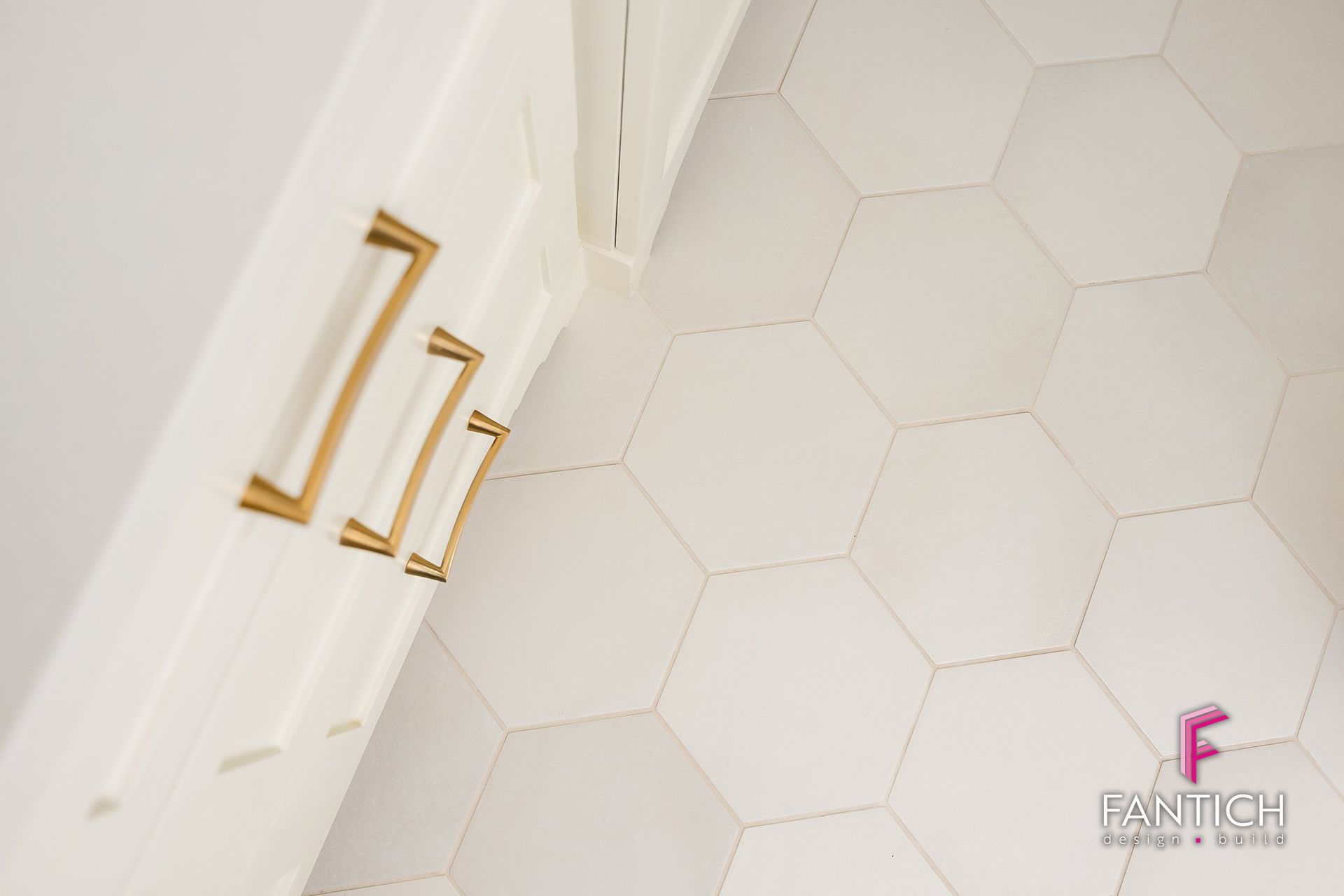 Gold handles on white cabinet doors beside a white hexagon-tile wall