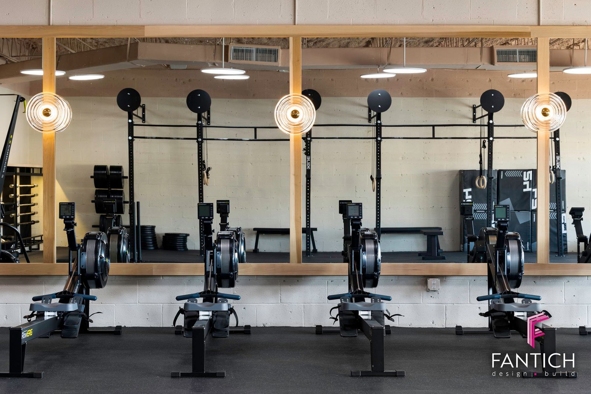 Indoor gym with four rowing machines lined up in front of a mirrored wall.