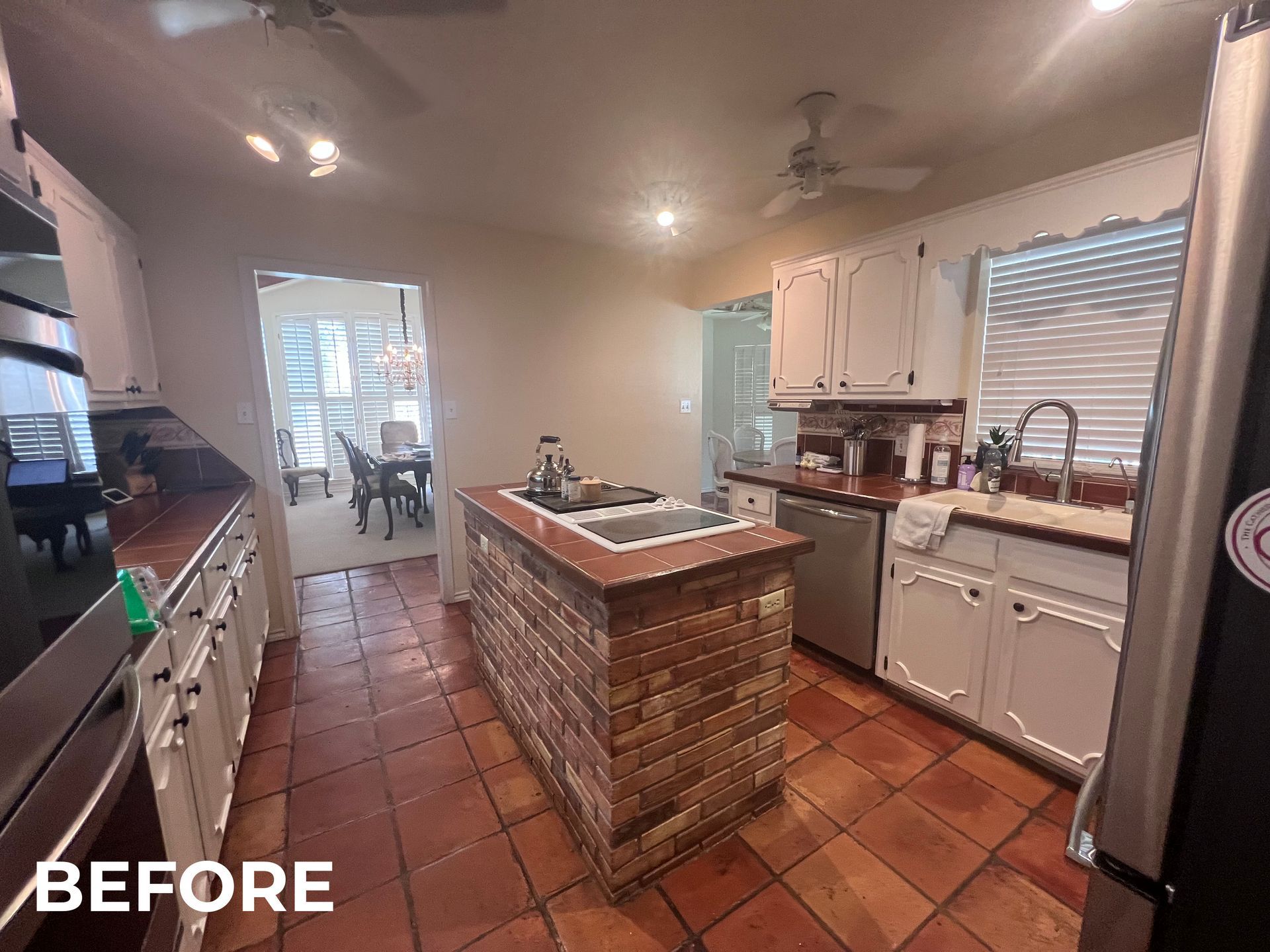Kitchen with brick island, white cabinets, tile floor, and a dining area in the background.