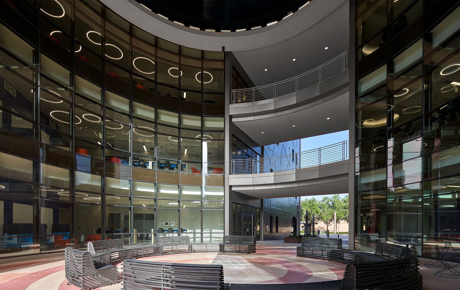 Modern glass atrium lobby with curved balconies, lounge seating, and sunlight streaming in