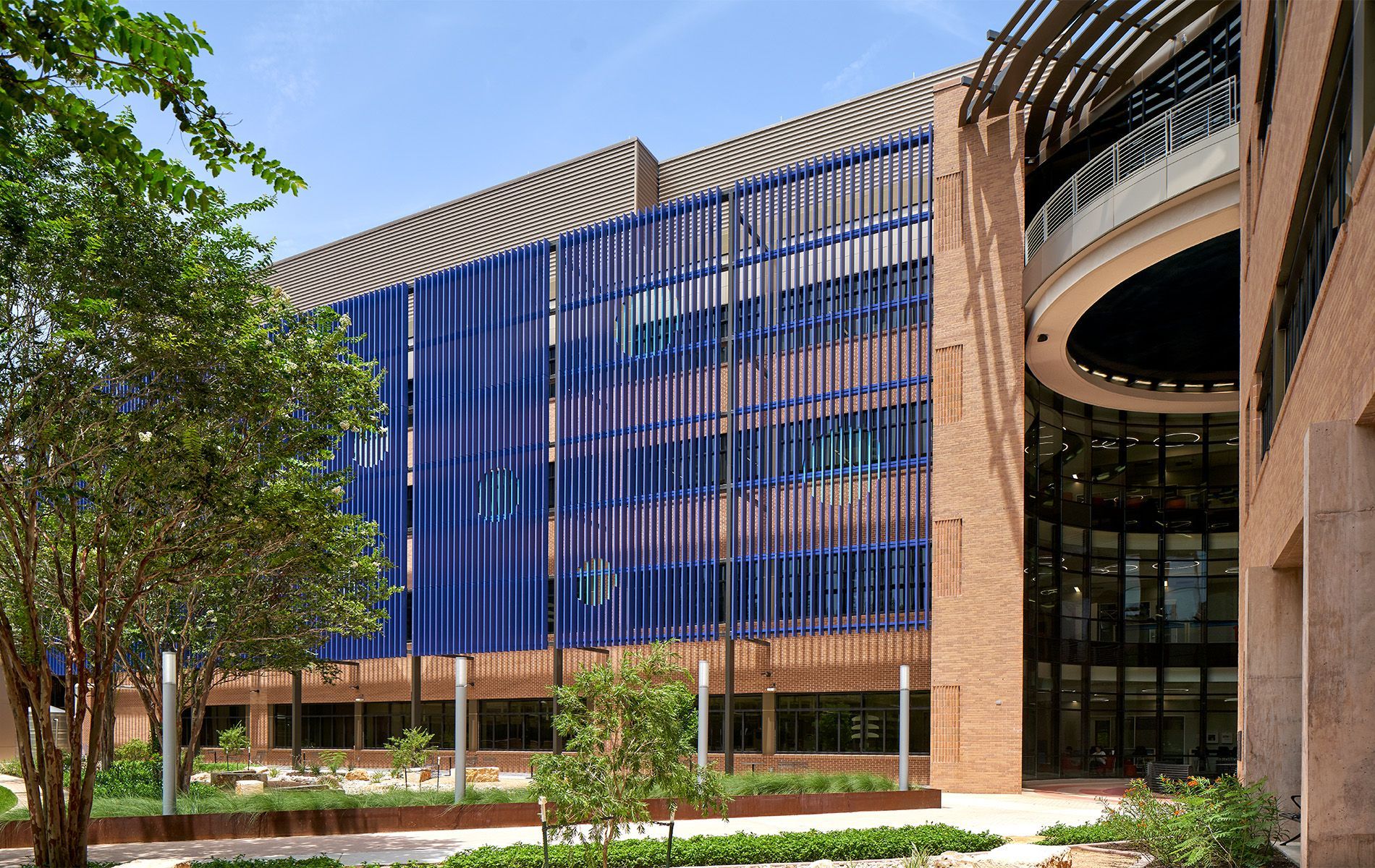 Modern building with blue glass facade, trees, and a curved entrance in a landscaped courtyard
