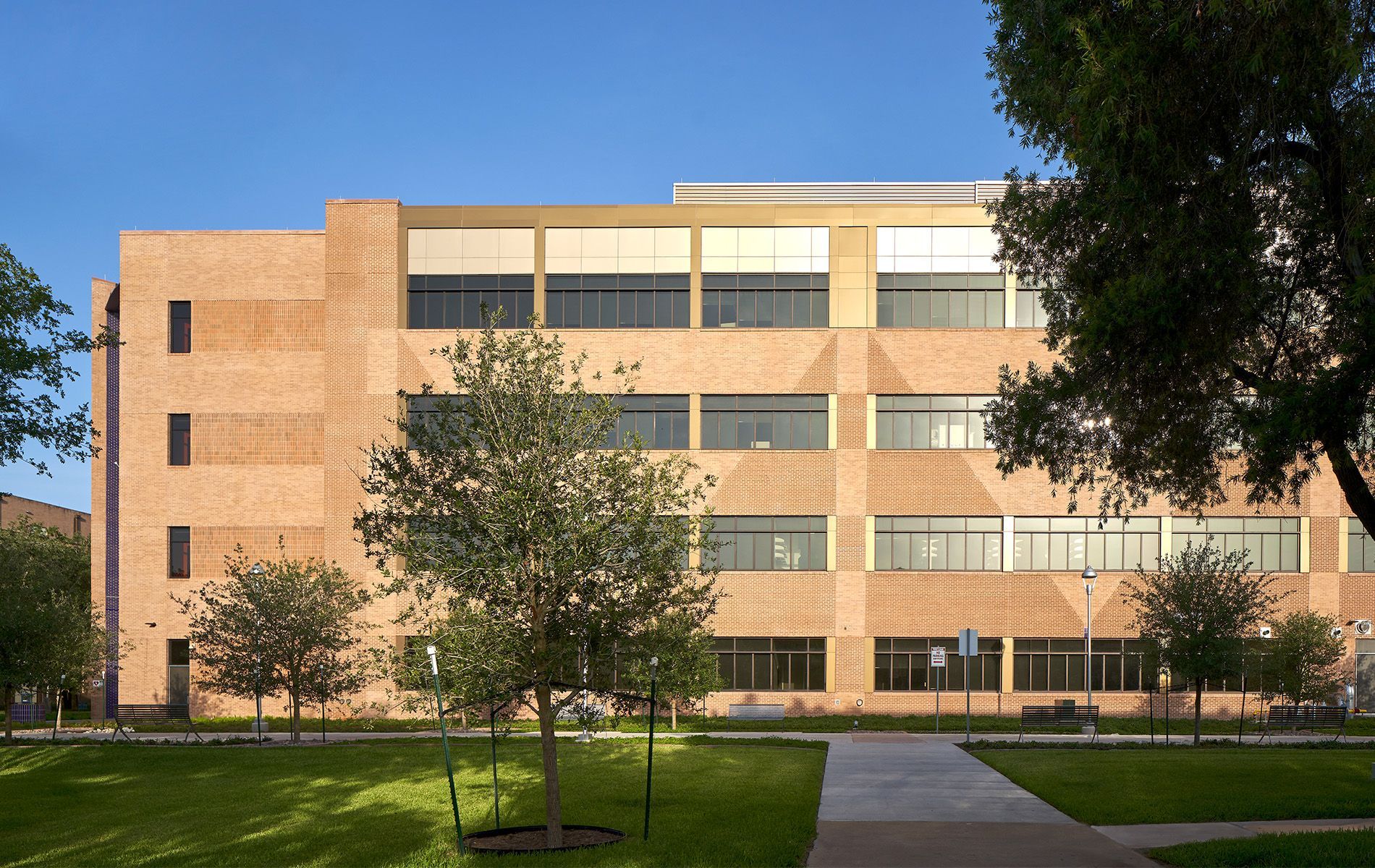 Three-story brick building with rows of windows, a lawn, and a tree-lined walkway at dusk