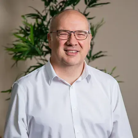 A bald man wearing glasses and a lanyard is smiling for the camera.