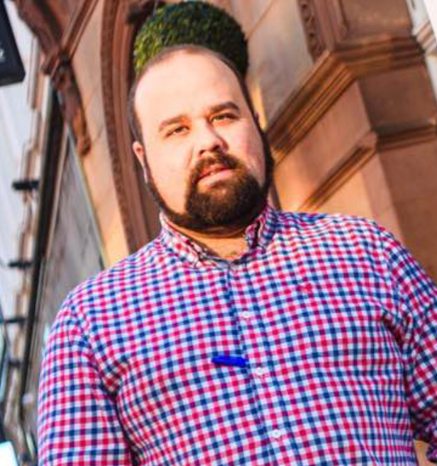 A man with a beard is standing at a bar holding a beer tap.