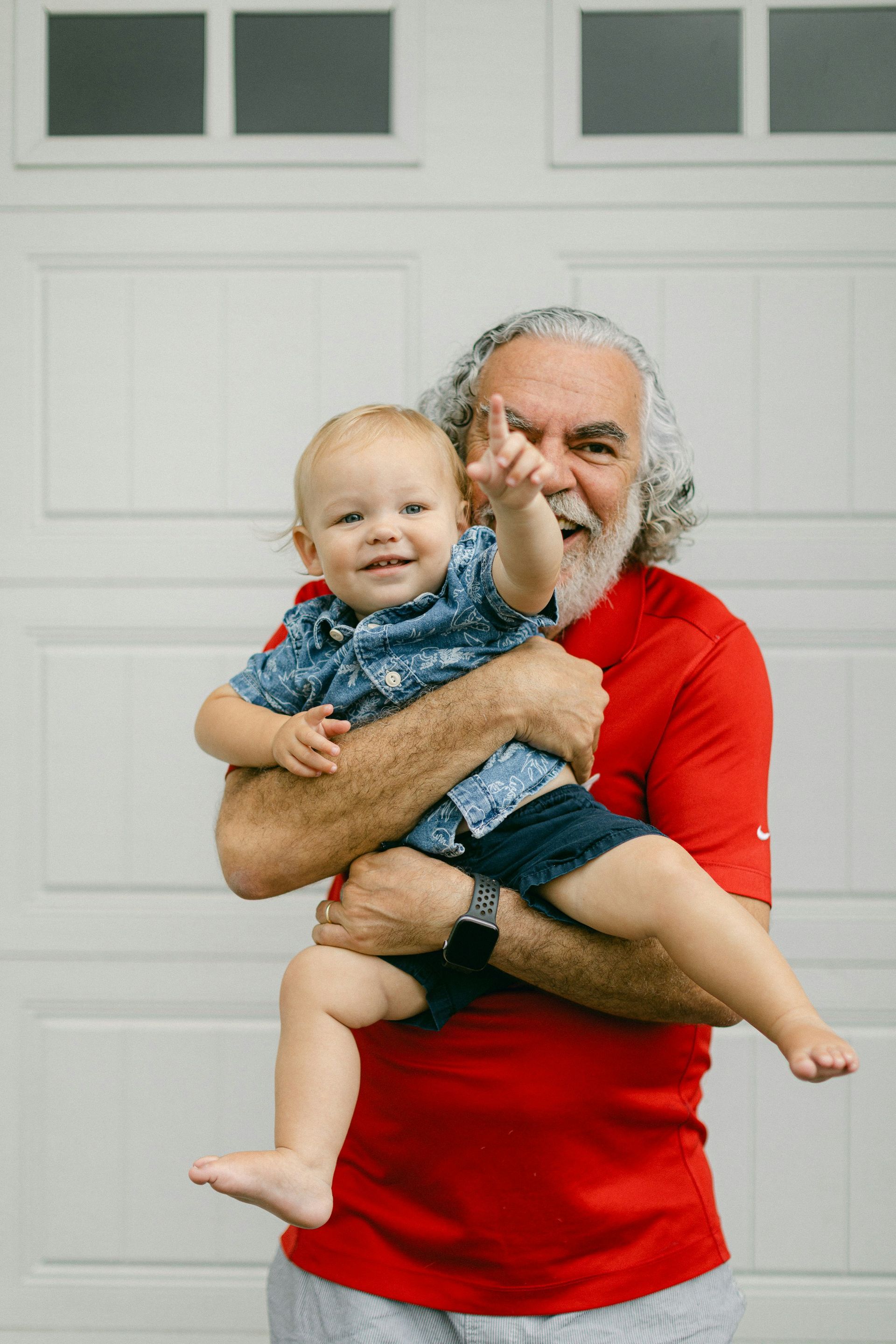 A man in a red shirt is holding a baby in his arms.