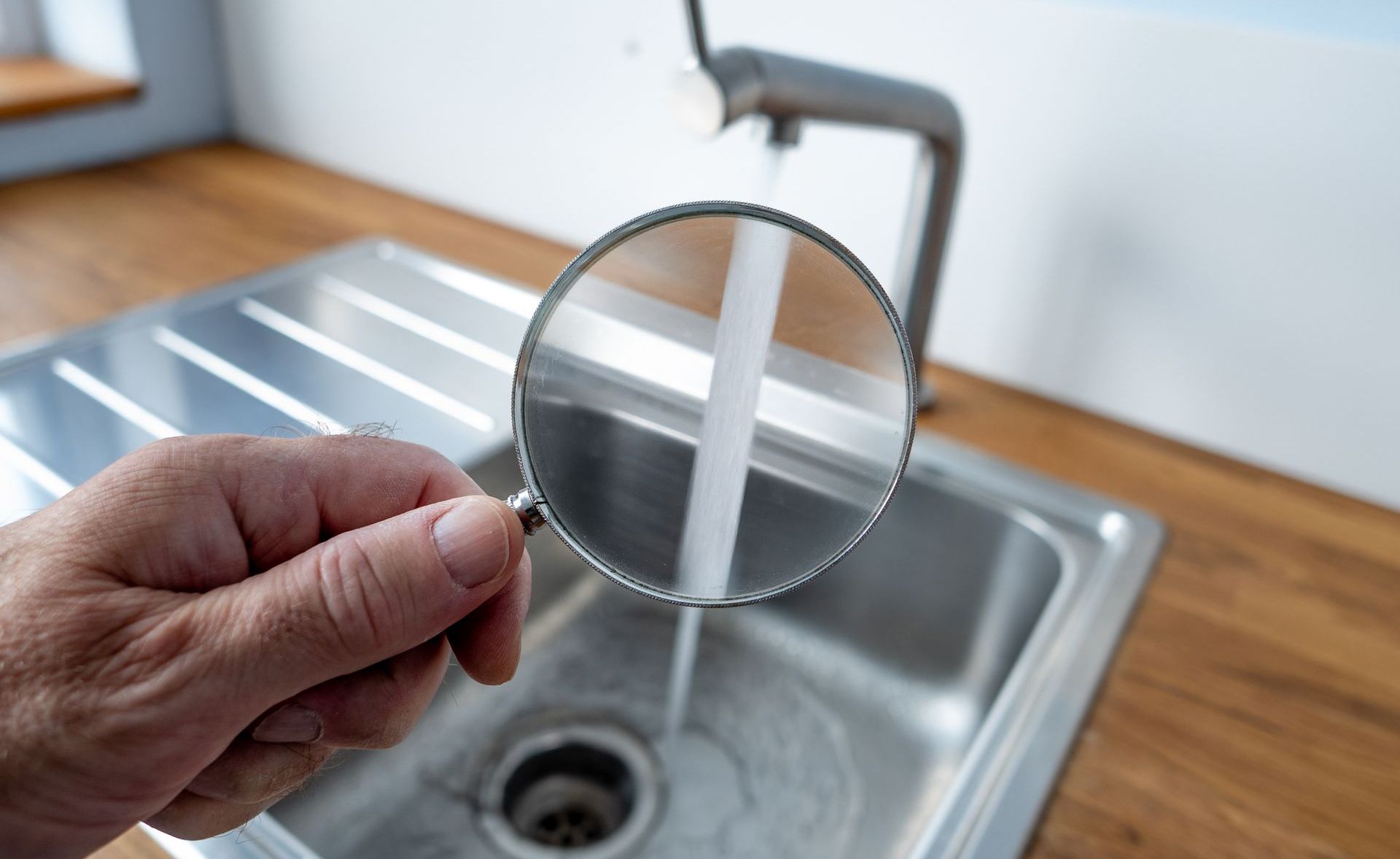 A person is holding a magnifying glass over a sink.