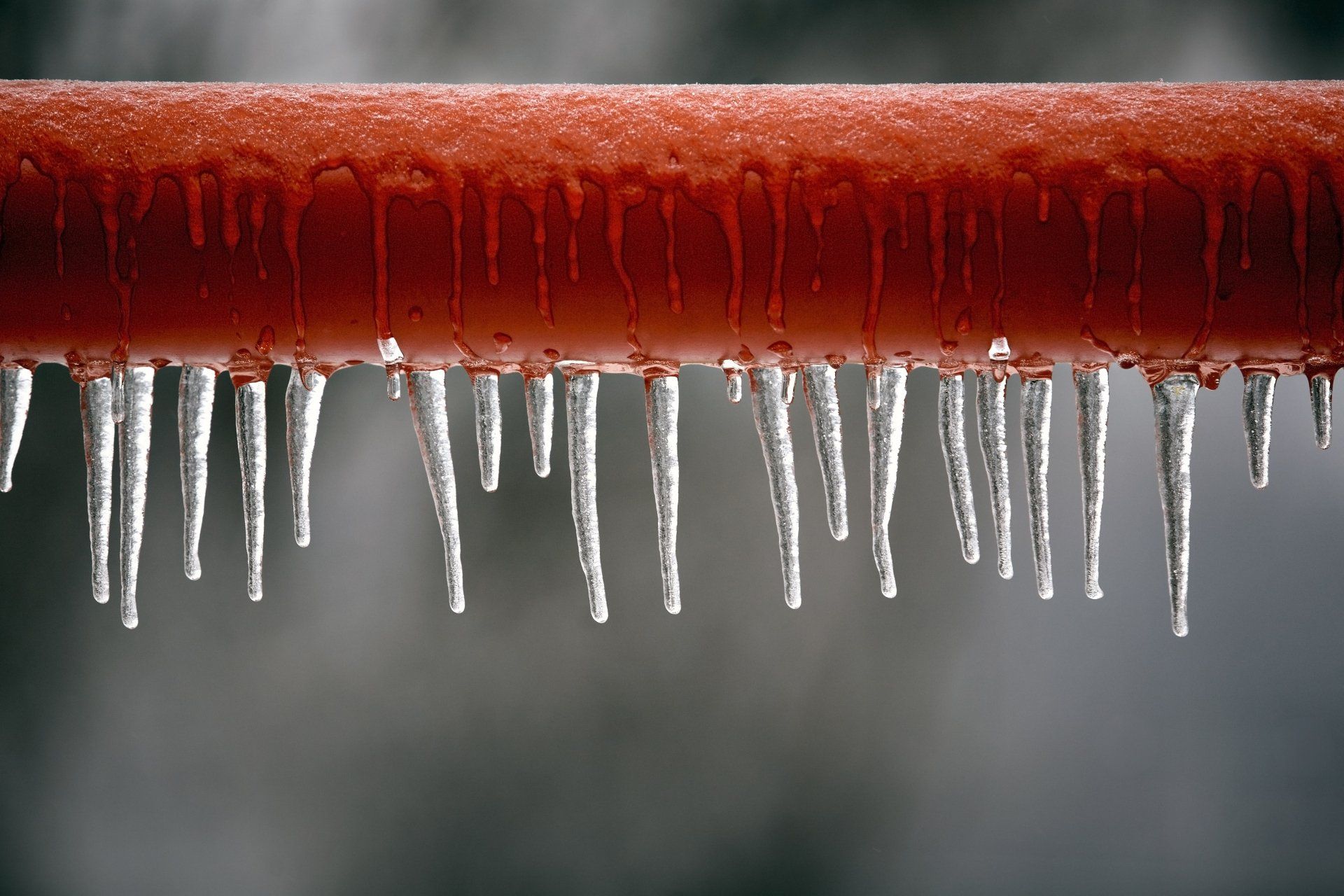 Icicles are hanging from a red pipe.