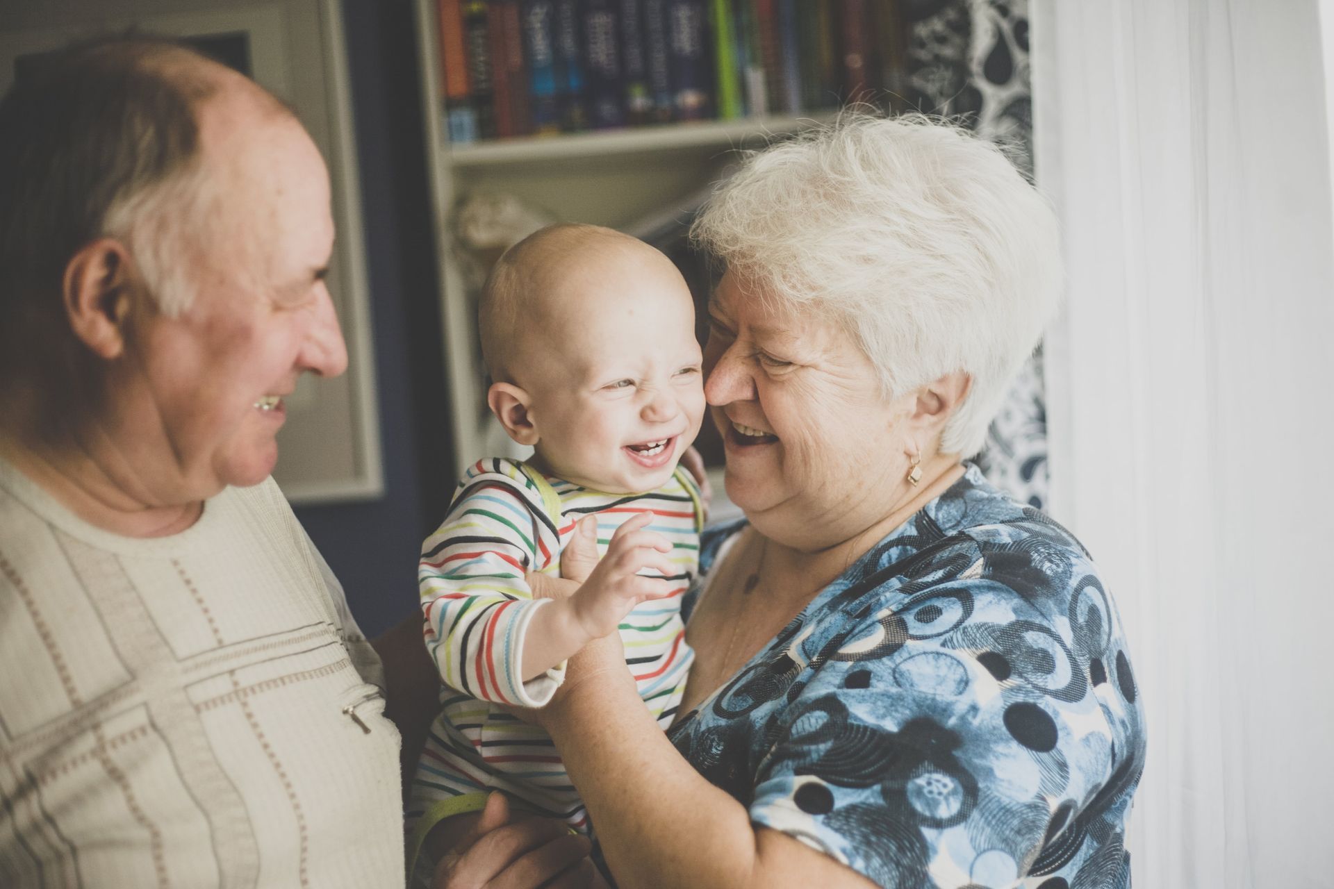 An elderly couple is holding a baby in their arms.