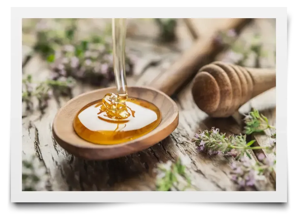 A jar of honey with a honey dipper next to a honeycomb