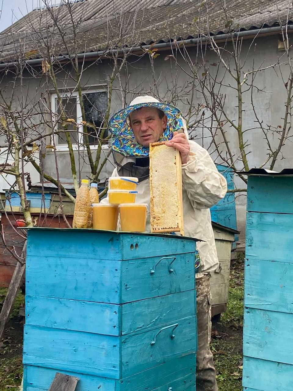A man is standing next to a beehive holding a honeycomb.