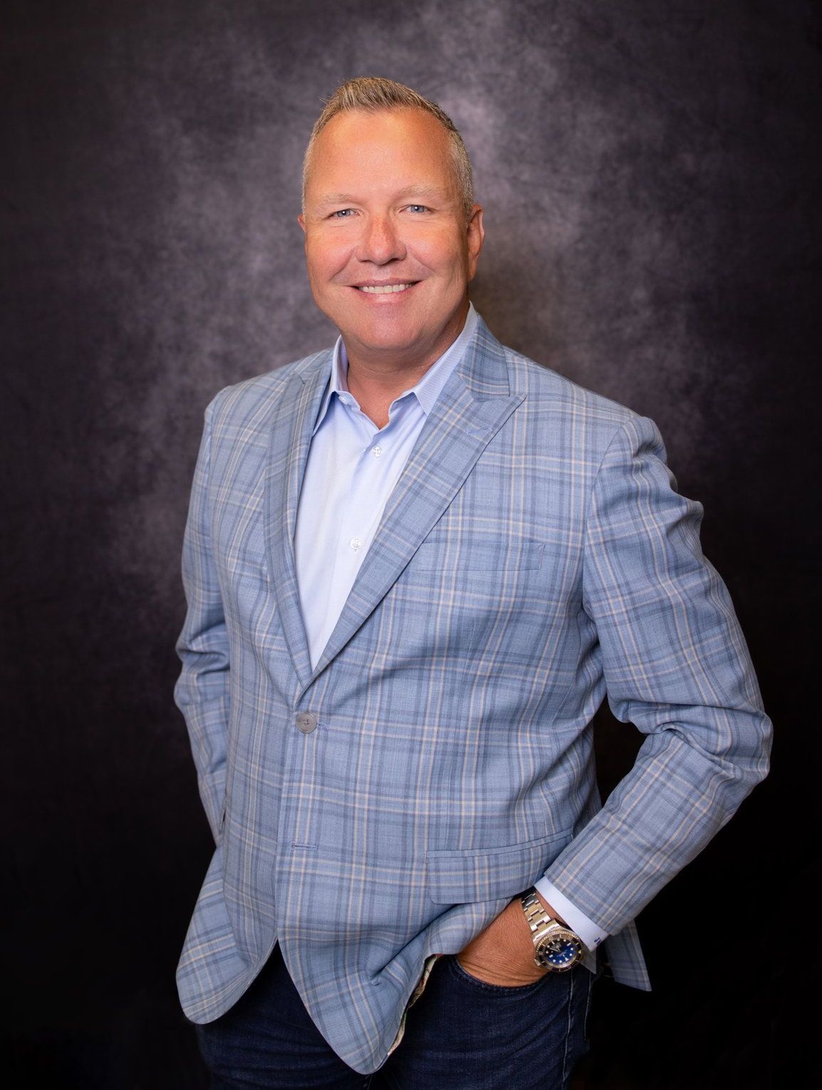 A man in a blue plaid jacket is standing with his hands in his pockets.