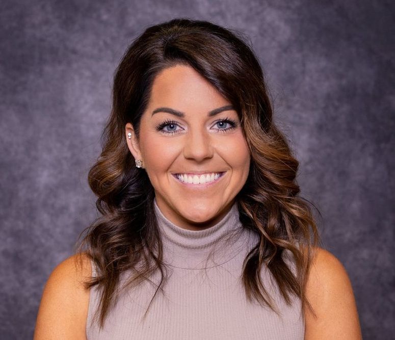 A woman is smiling for the camera and wearing a turtleneck sweater.