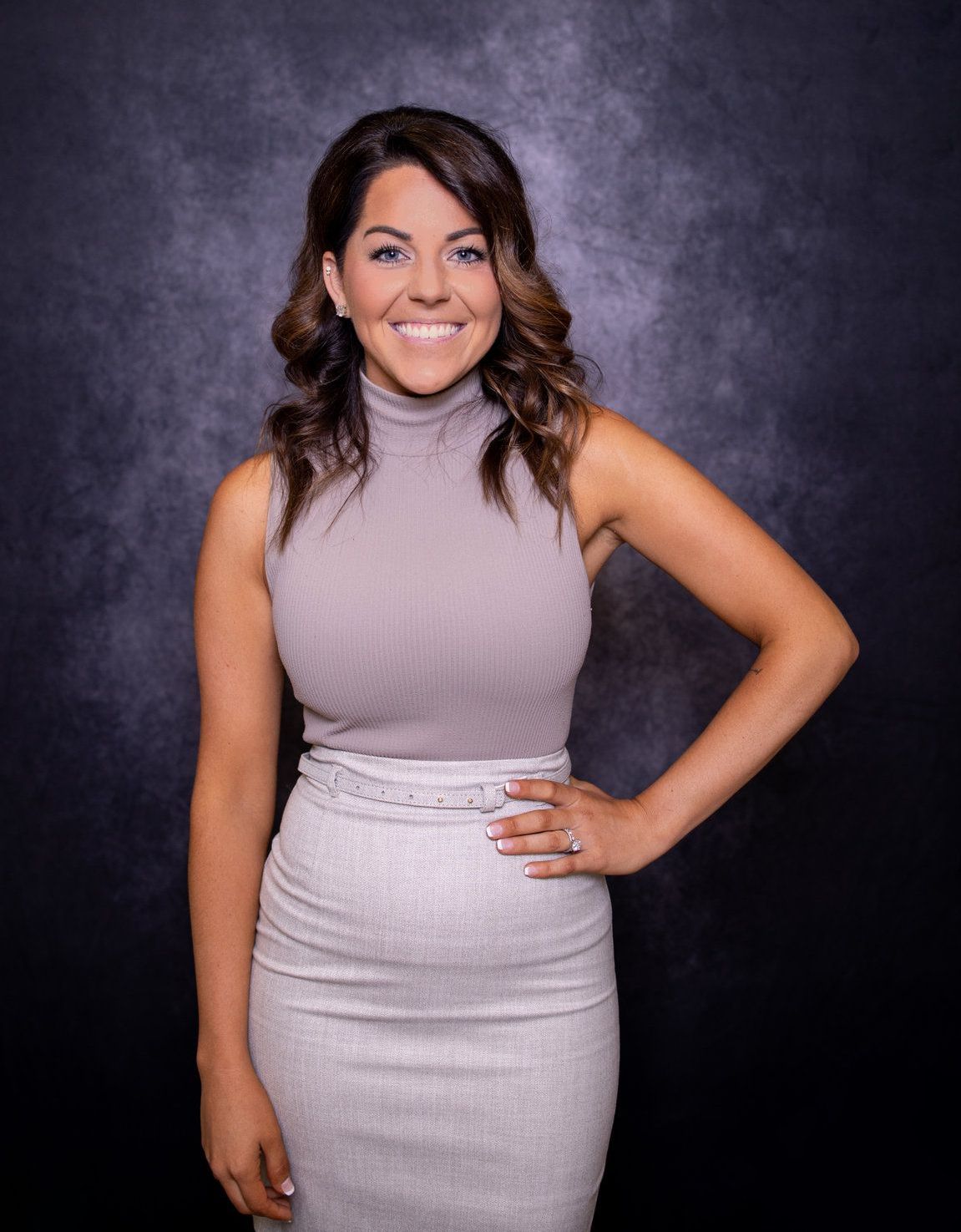 A woman is standing in front of a black background with her hand on her hip.