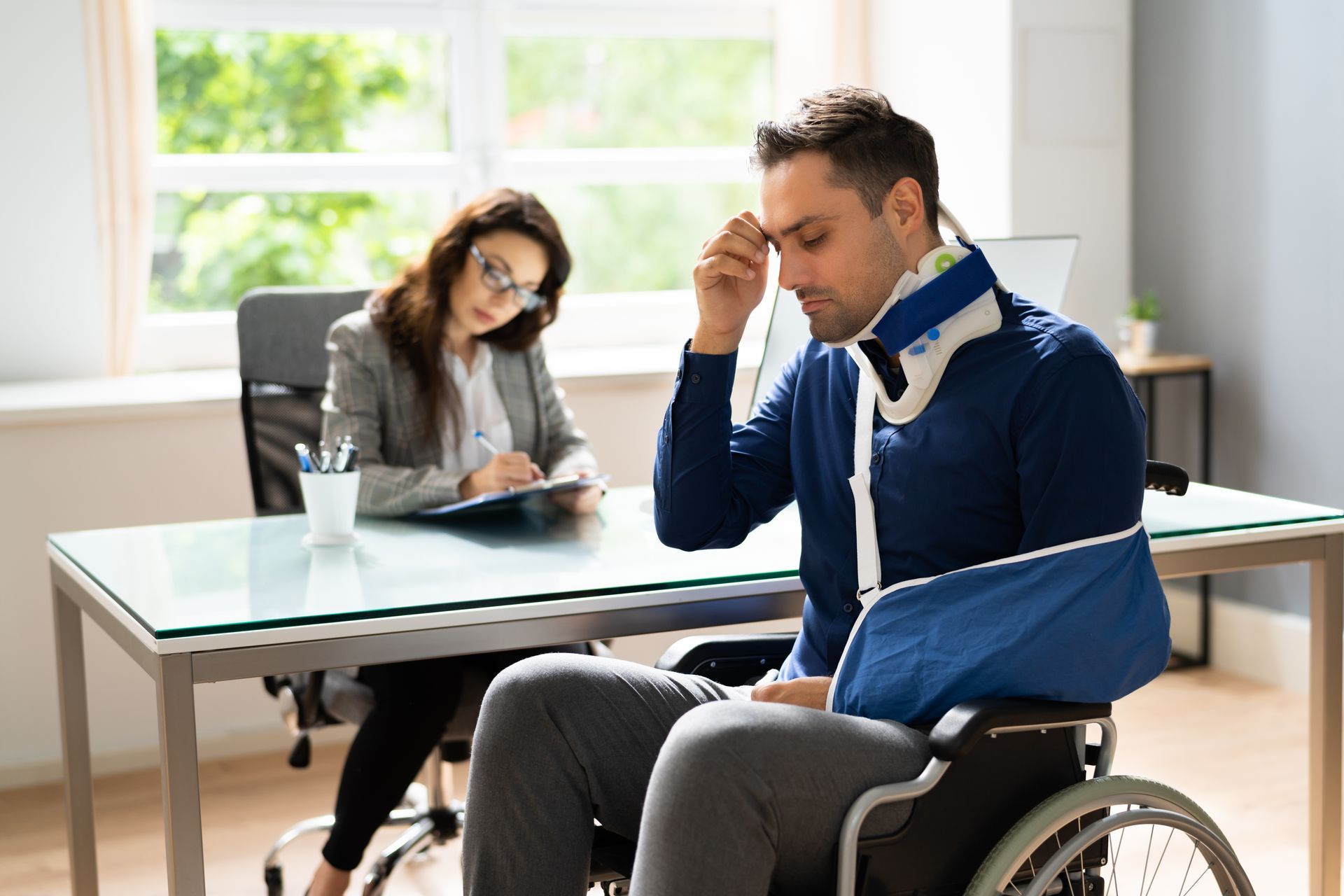 A man in a wheelchair with a broken arm is sitting at a desk with a woman.