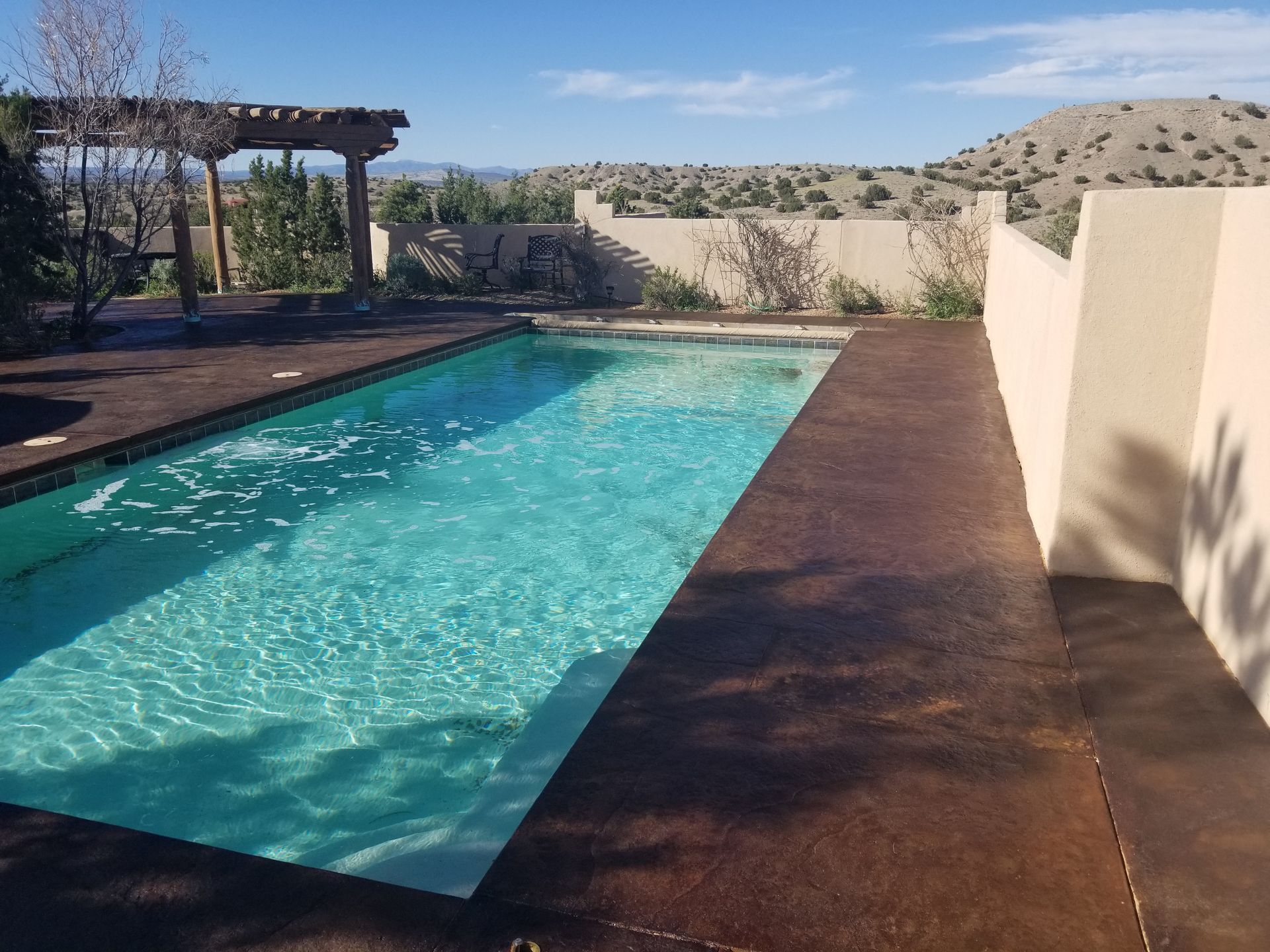Pool and patio under a rainbow at sunset, with a cloudy sky and lounge chairs.