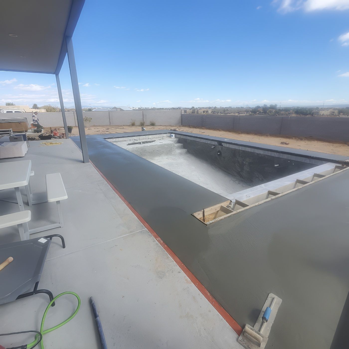 Rooftop under construction with a rectangular pool, gray deck, and blue sky overhead