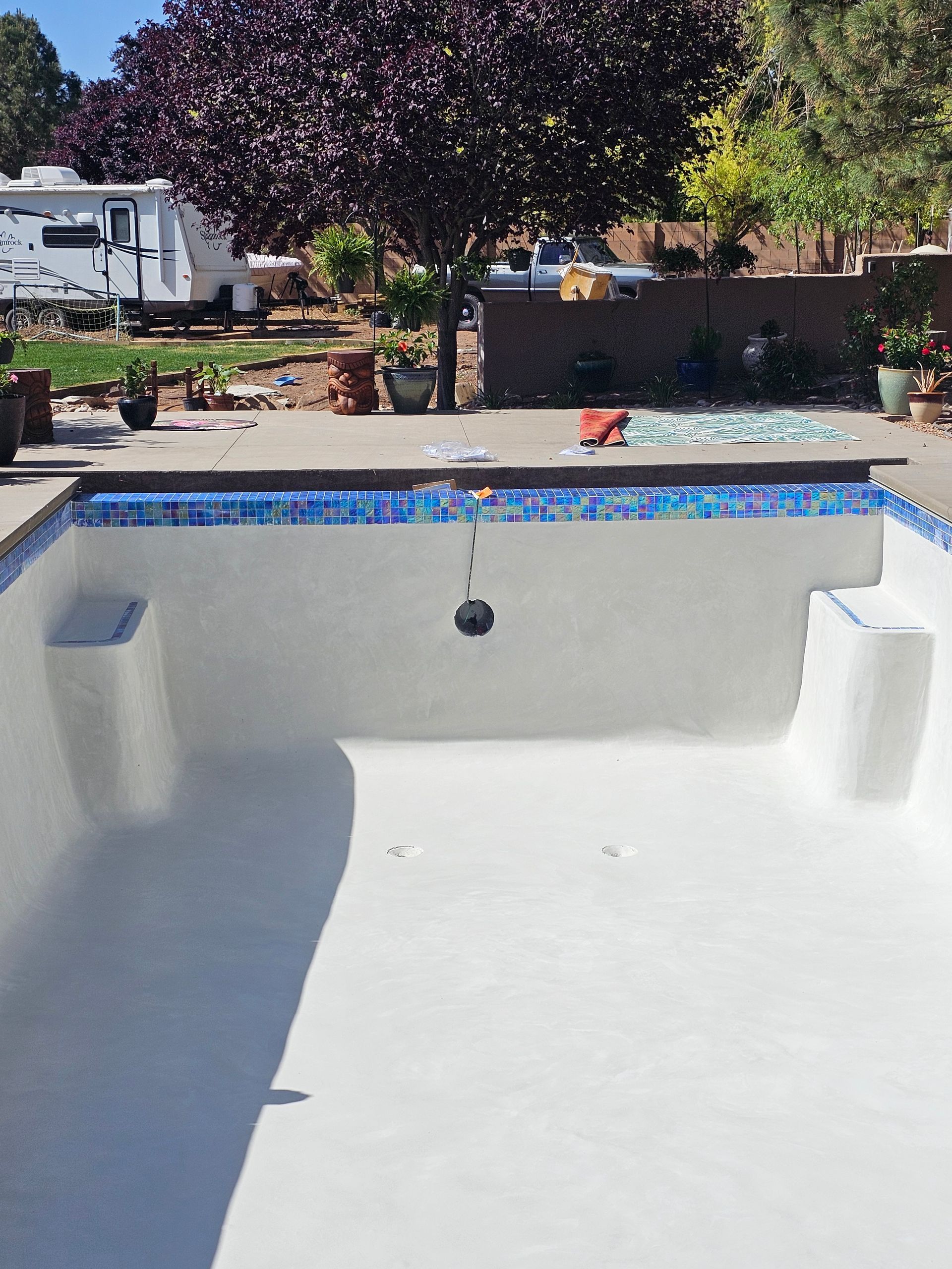 A robotic black pool cleaner scrubbing the shallow end of a bright blue tiled swimming pool.