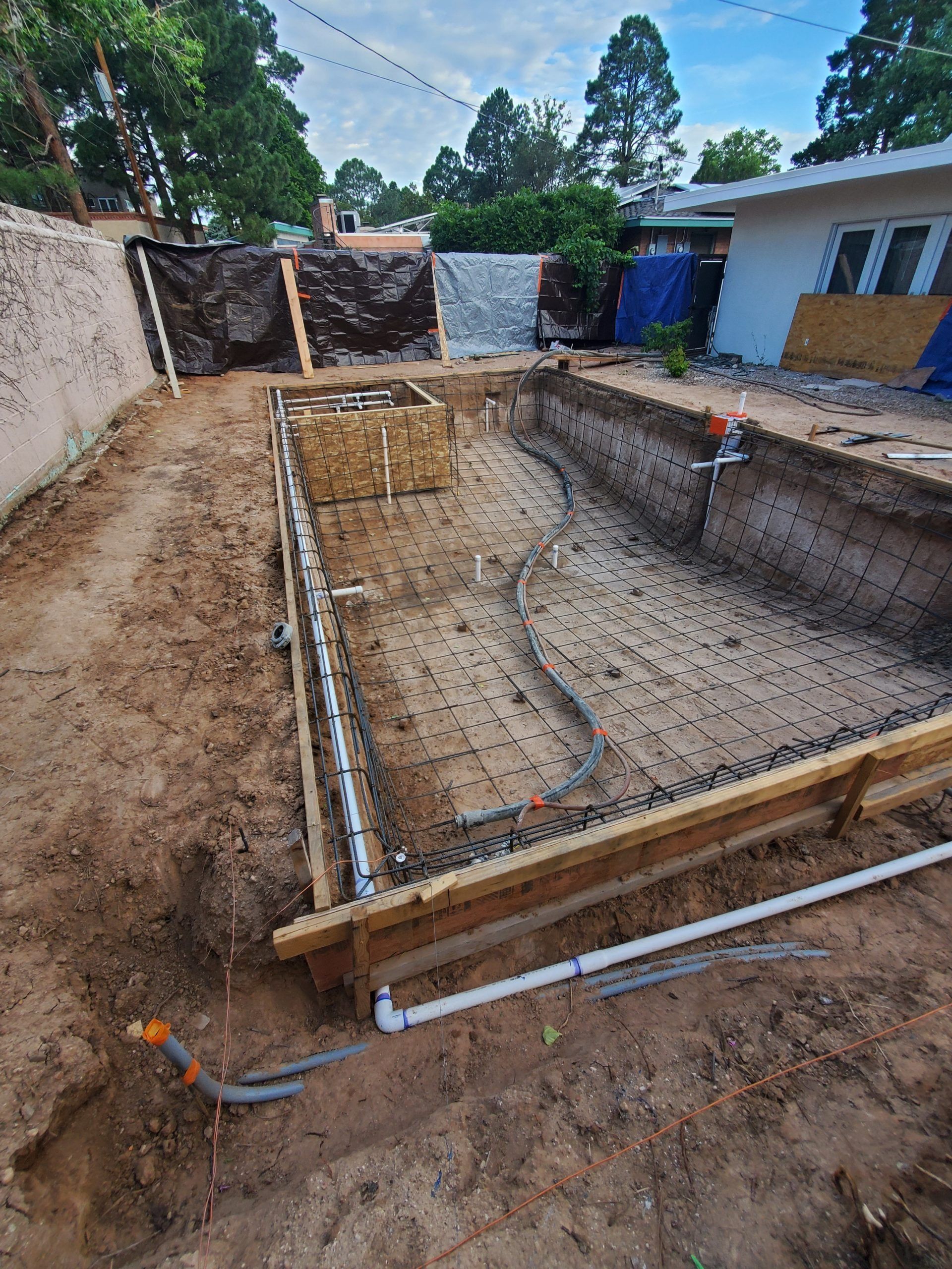 Excavated backyard foundation with rebar, concrete footings, and surrounding dirt at a construction site
