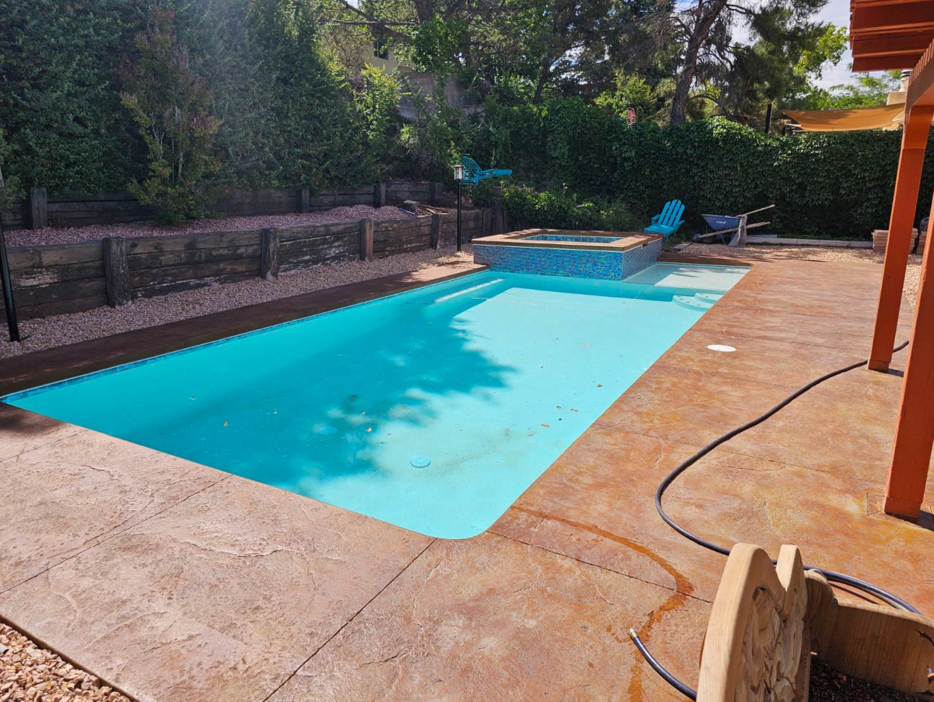 Backyard swimming pool with turquoise water, concrete deck, trees, and lounge chairs in shade