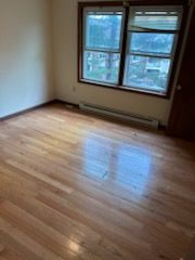 Empty room with hardwood floors, a window, and a baseboard heater.