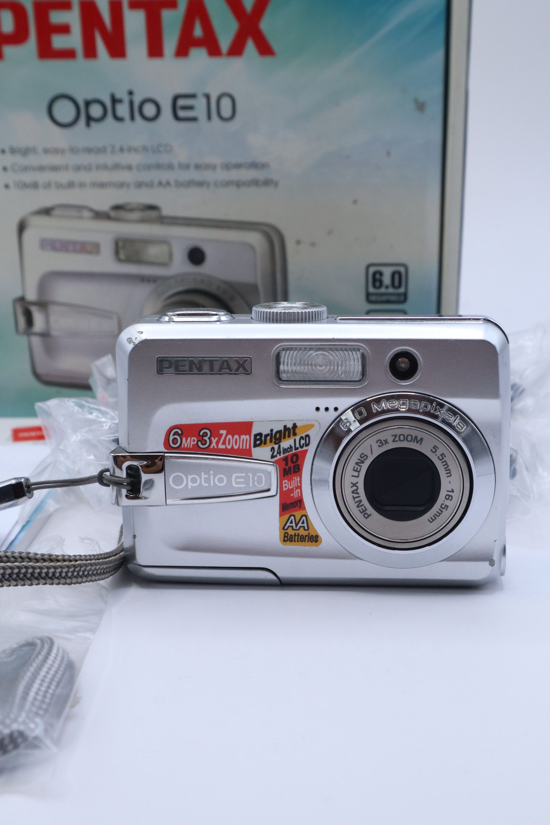 Pentax Optio E10 camera box with silver digital camera, CD, cable, and accessories laid out on a white surface