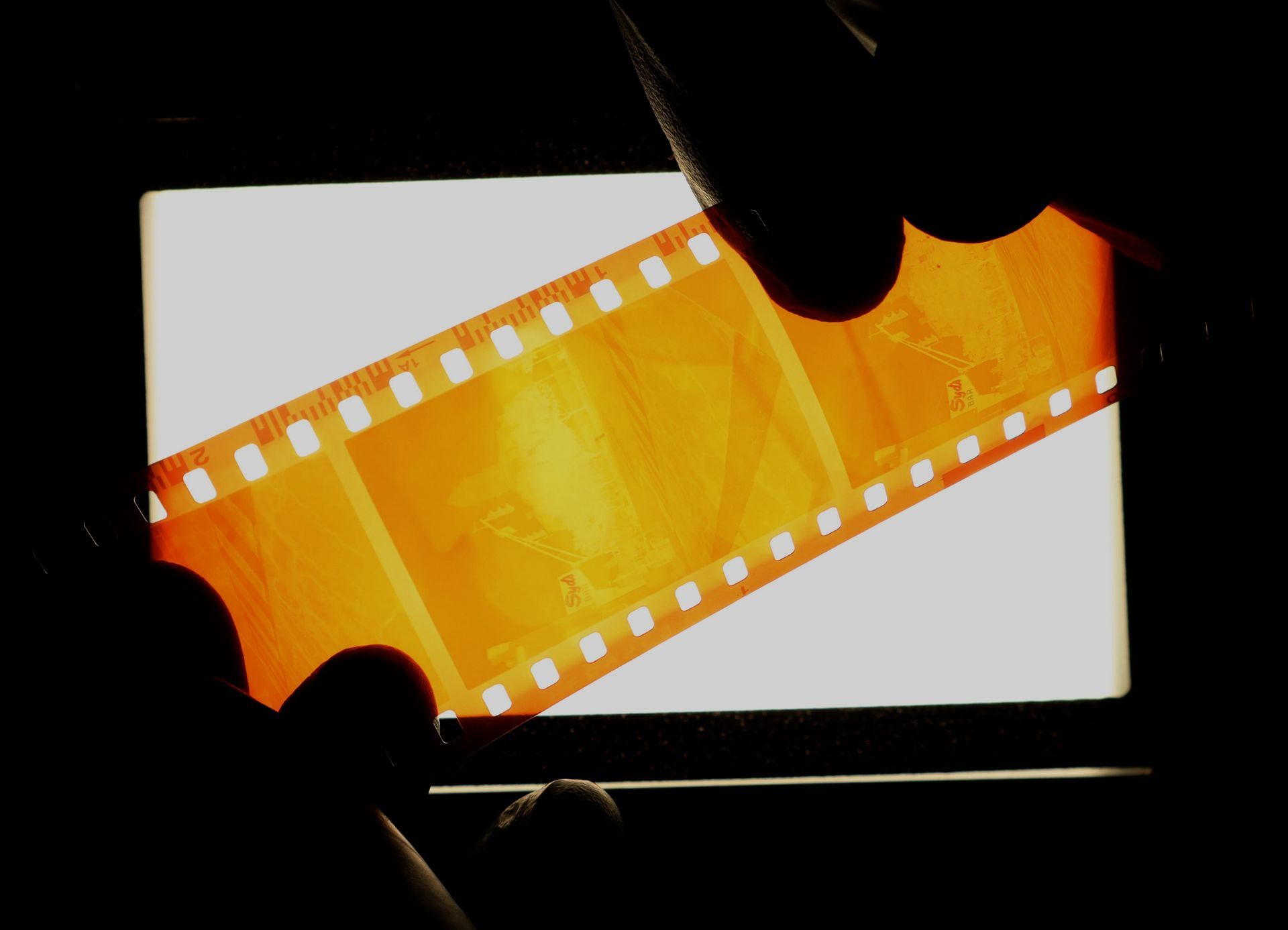 Orange film strip held against a bright white background by silhouetted hands