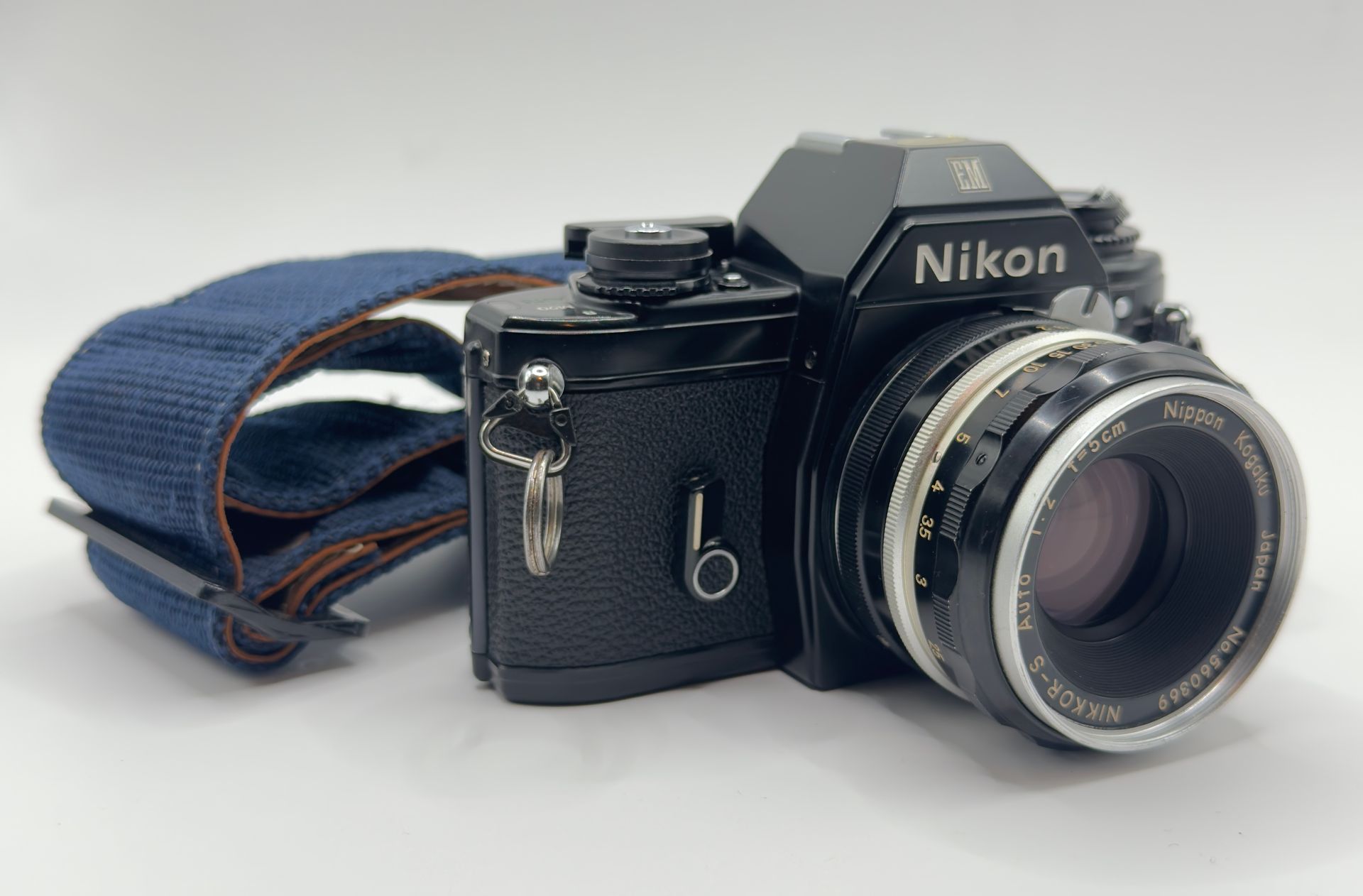 Black Nikon film camera with silver lens and blue strap on a white background