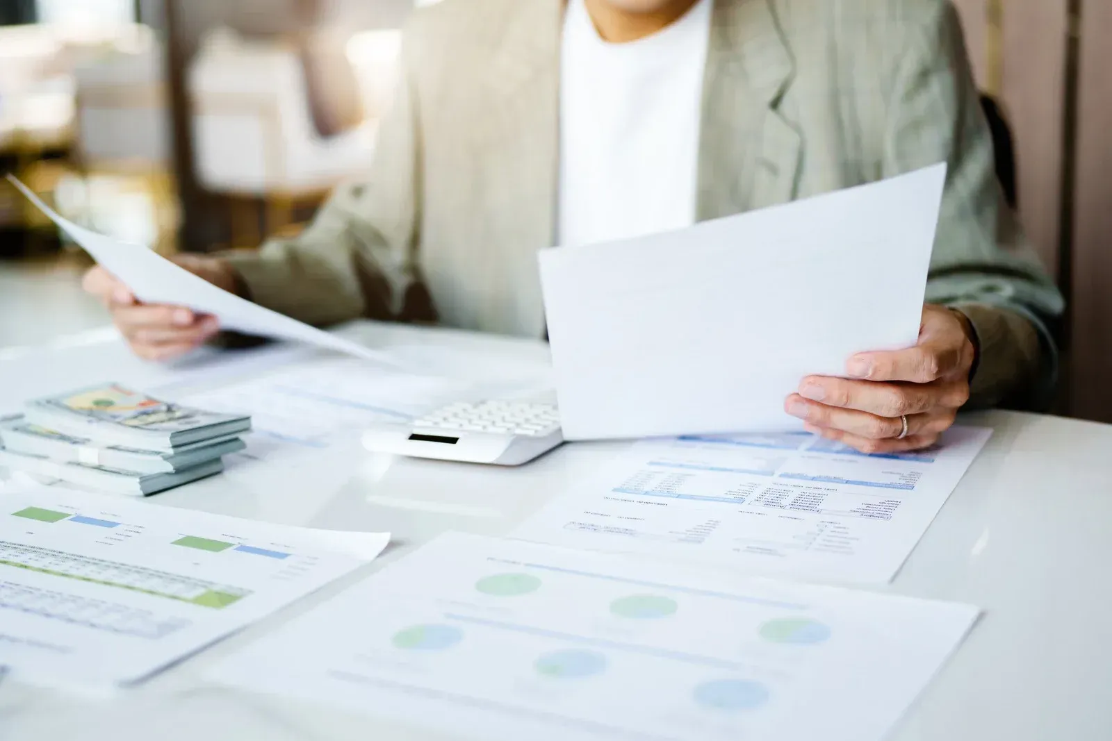 Person in a suit reviews documents at a desk, papers and money visible.