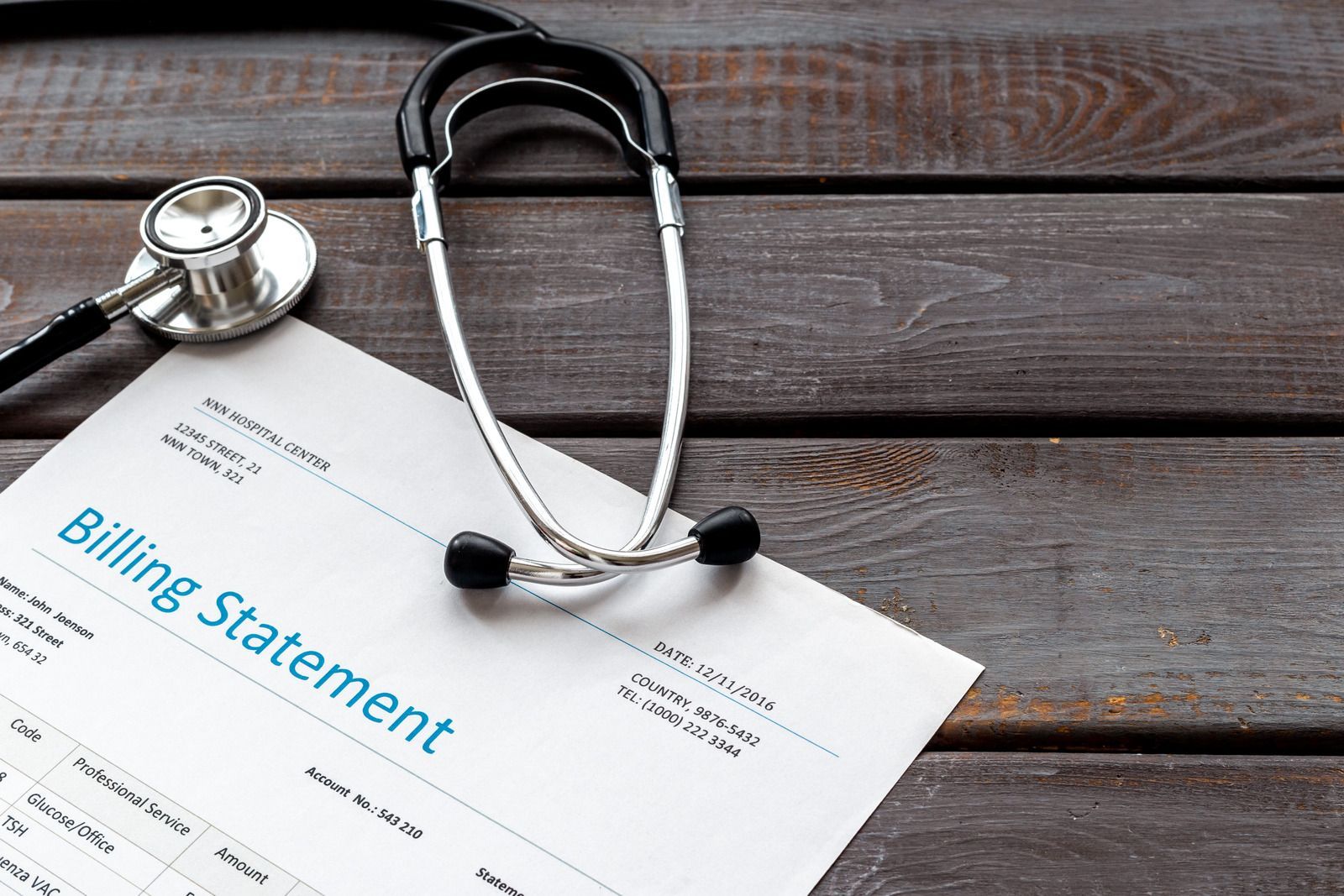 Billing statement and stethoscope on a dark wooden surface.