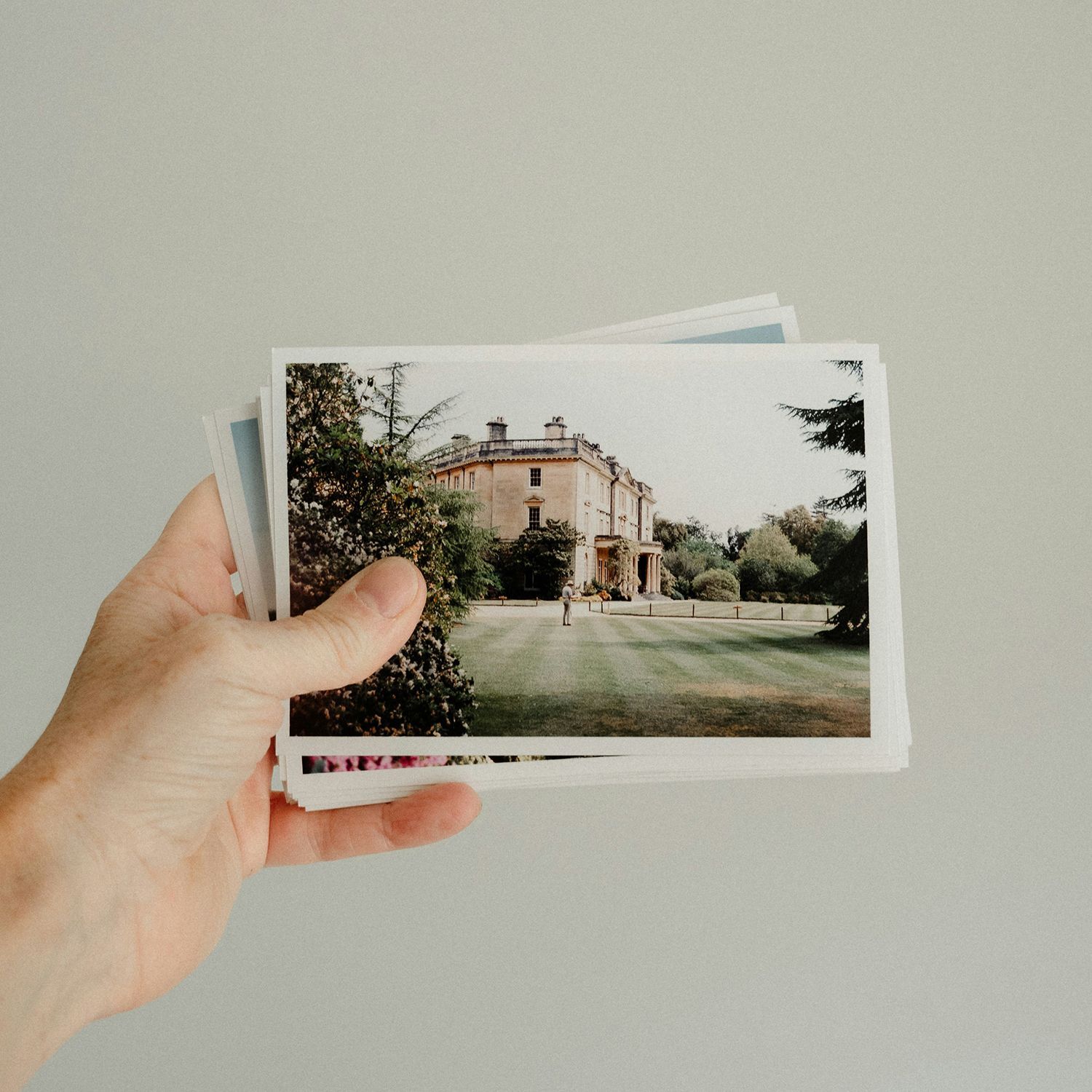 Hand holding a stack of small photos, top one showing a building and lawn outdoors