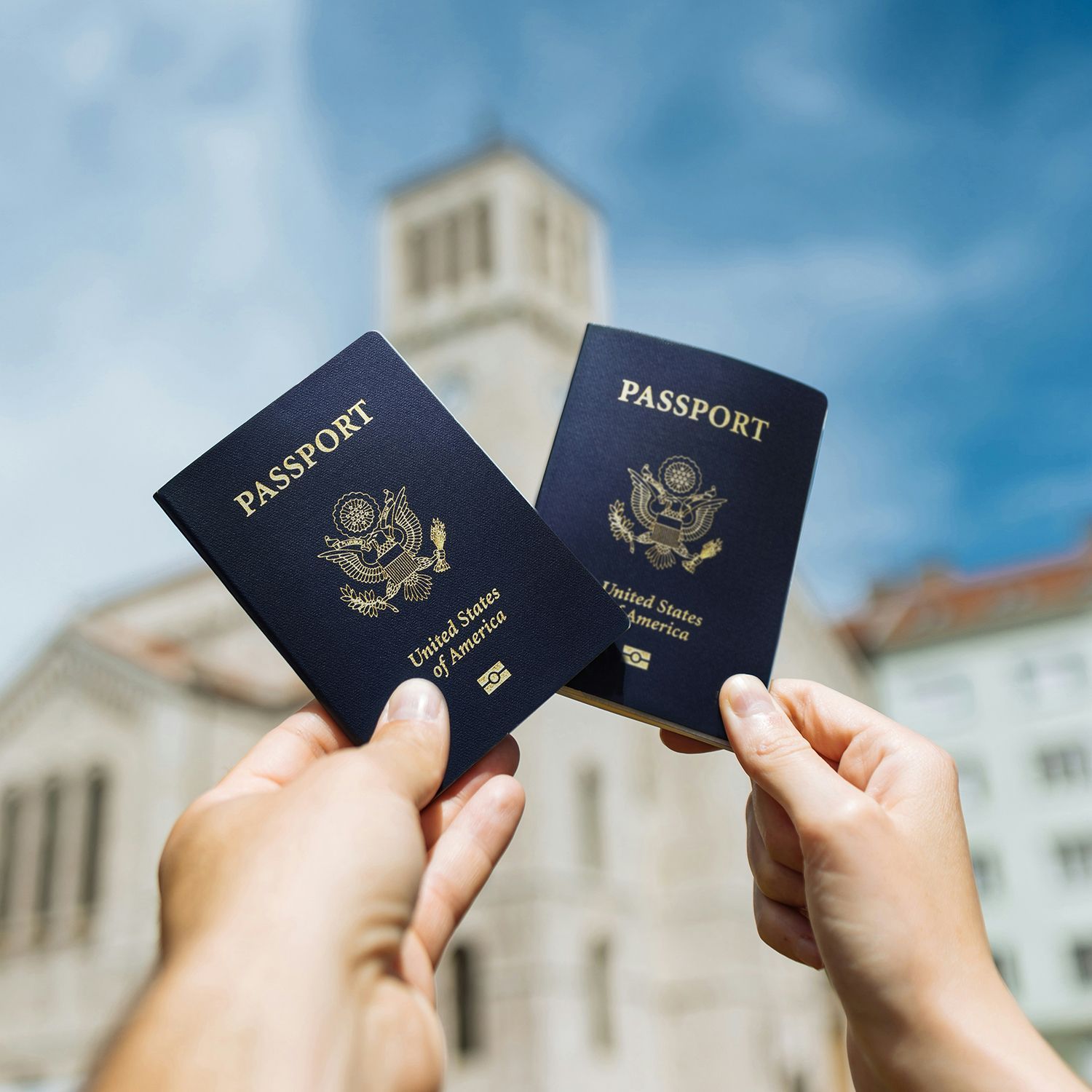Two passports held up against a blurred city building and blue sky.