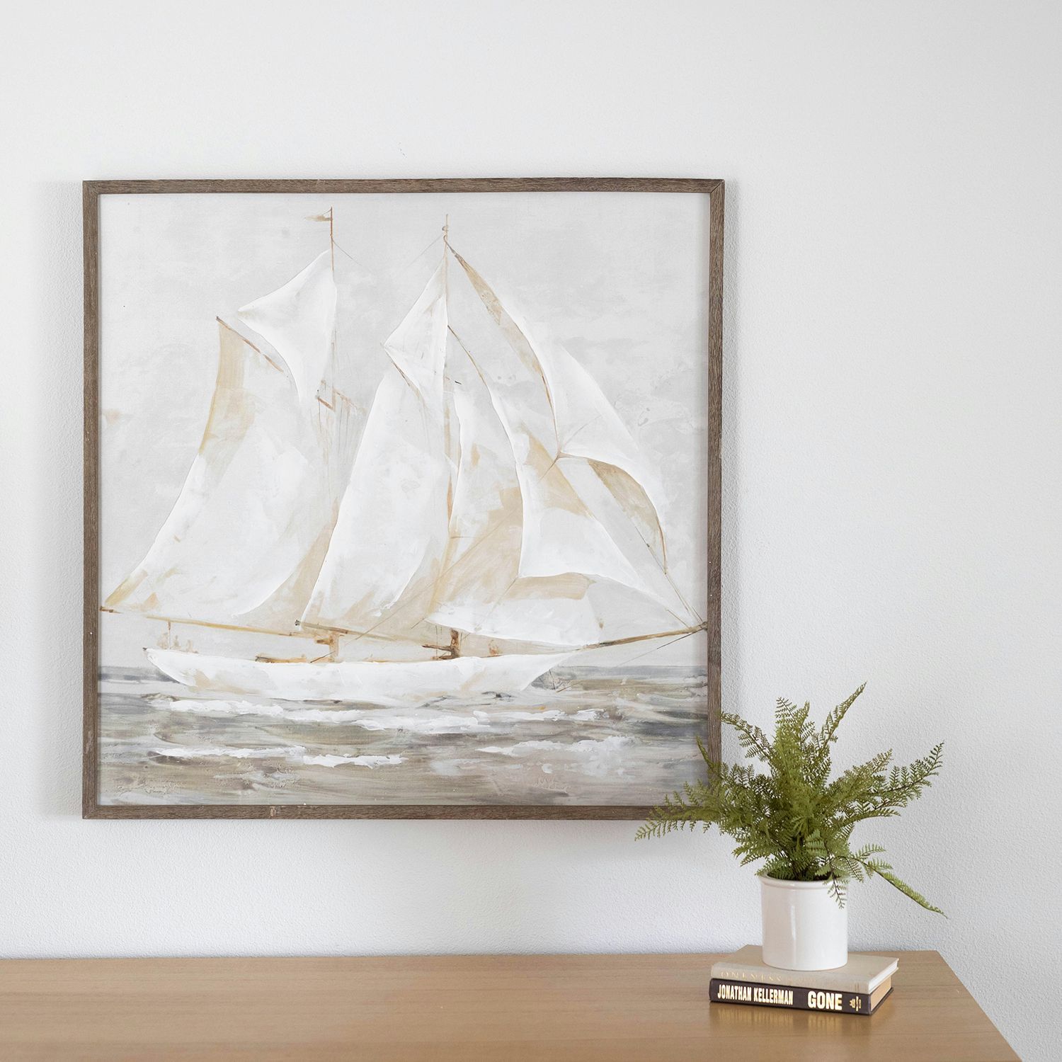 Framed sailboat painting above a wooden console with a white vase and greenery
