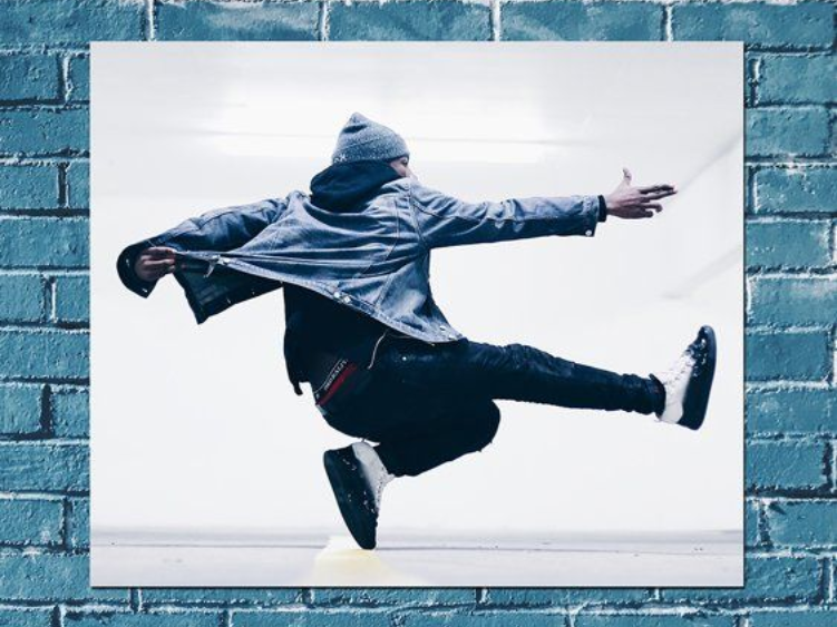Person in a hoodie mid-jump against a blue brick wall, arms and legs outstretched.