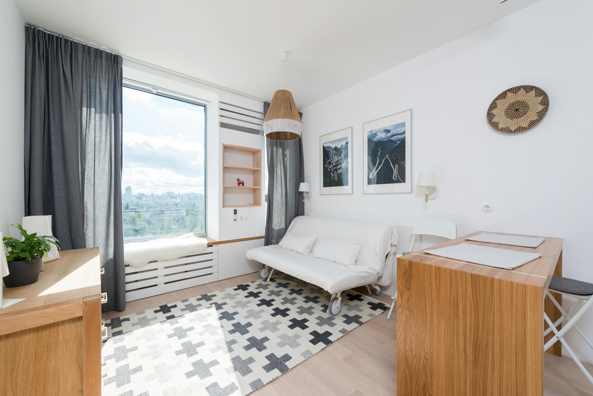 Bright minimalist bedroom with white sofa bed, patterned rug, desk, curtains, and large window.