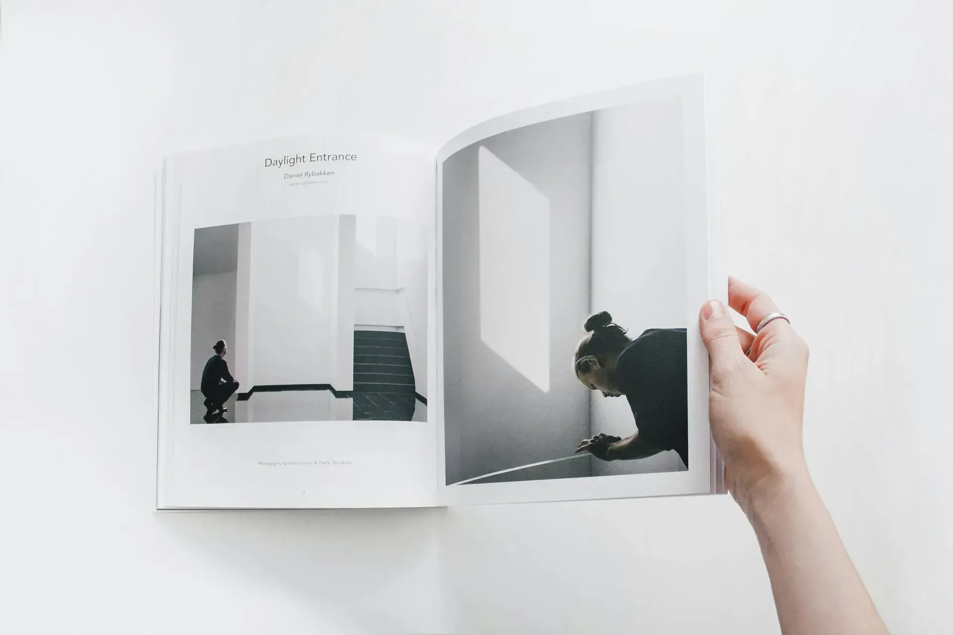 Hand holding an open book with minimalist black-and-white room photos on the pages